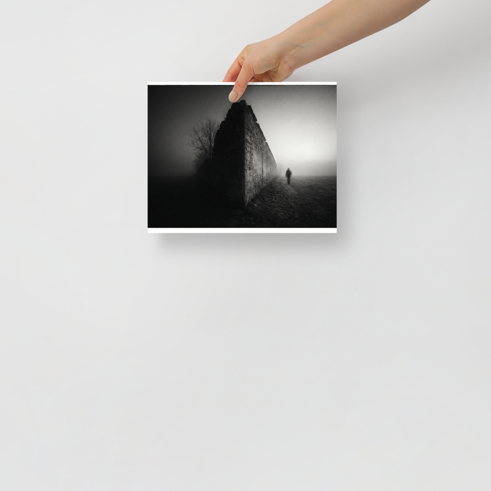 'Echoes in the Mist' — a Art photography print. A moody black and white photograph of a lone figure walking into dense fog next to an old stone wall, ideal for a modern Office or Den.