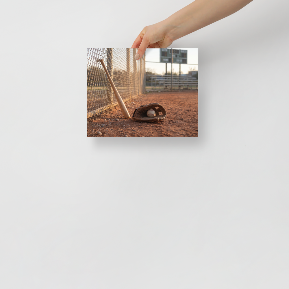 'Field of Memories' — a Art photography print. A photograph of a baseball bat leaning against a fence next to a glove and ball on a dirt field at sunset, a nostalgic piece for a Game Room.