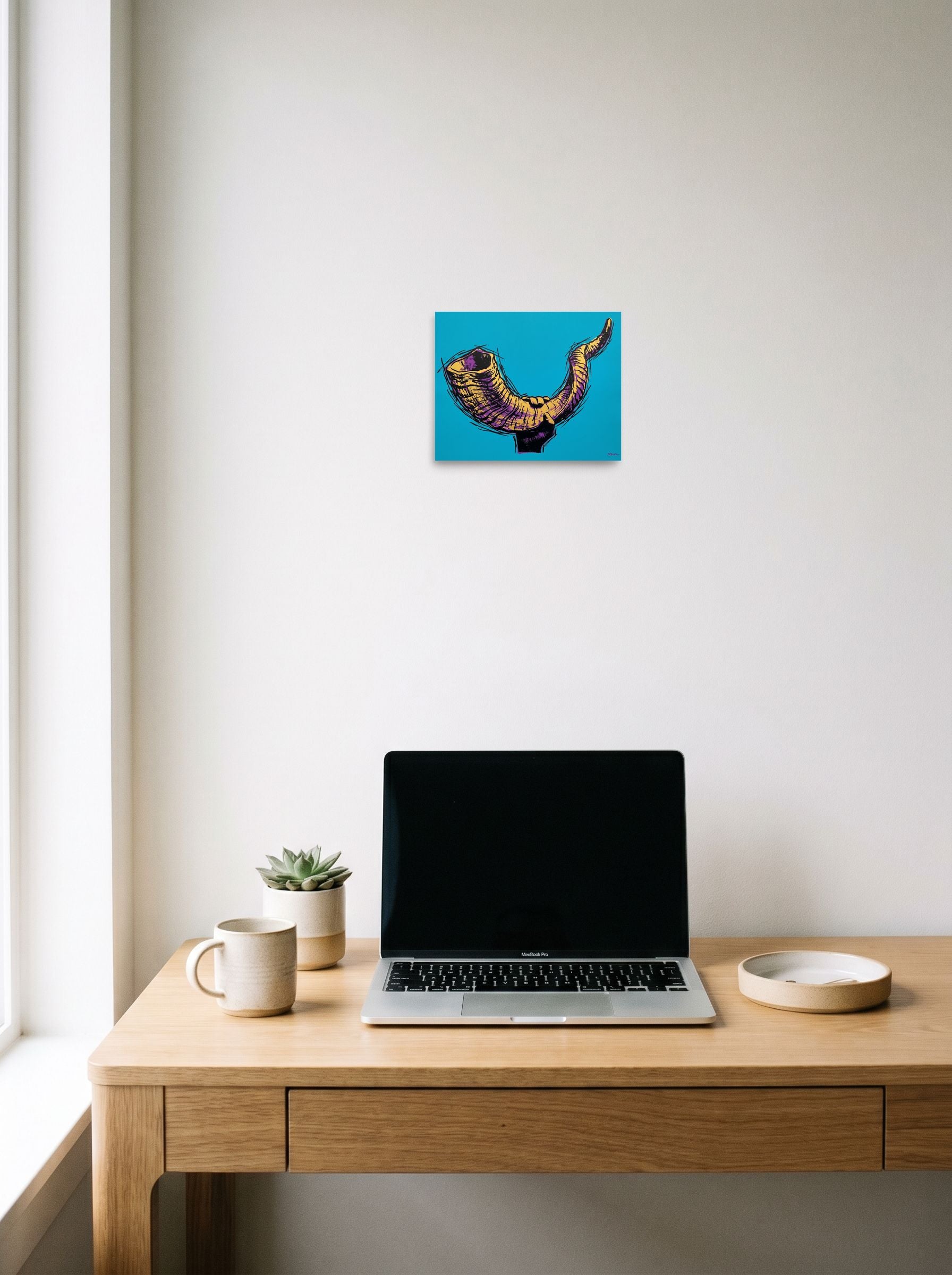 A 10x8 inch unframed paper Pop art print of 'The Golden Shofar' hanging above a worktable with a laptop.