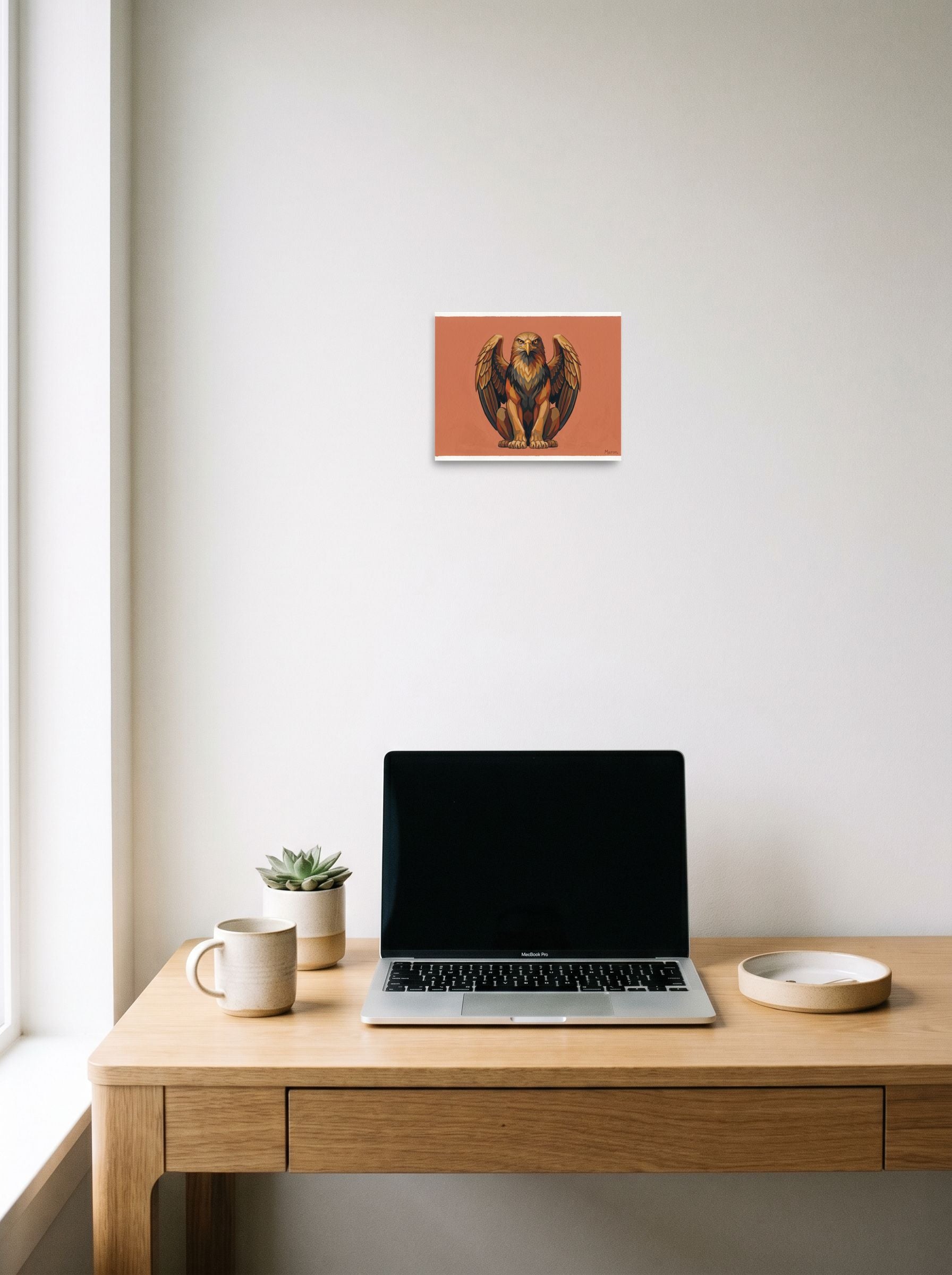 A 10x8 inch unframed paper Art Deco print of 'The Golden Griffin' hanging above a worktable with a laptop.