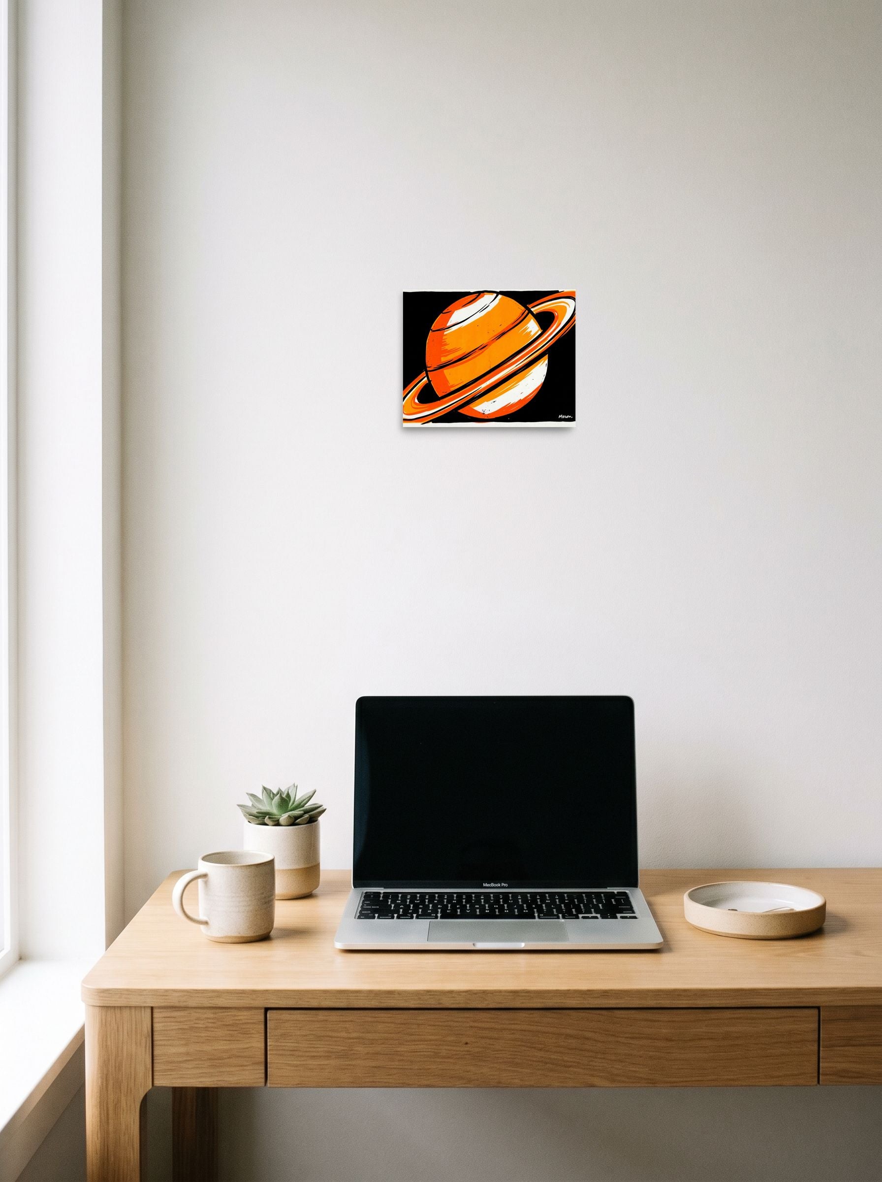 A 10x8 inch unframed paper Pop art print of 'Orange Orbit' hanging above a worktable with a laptop.