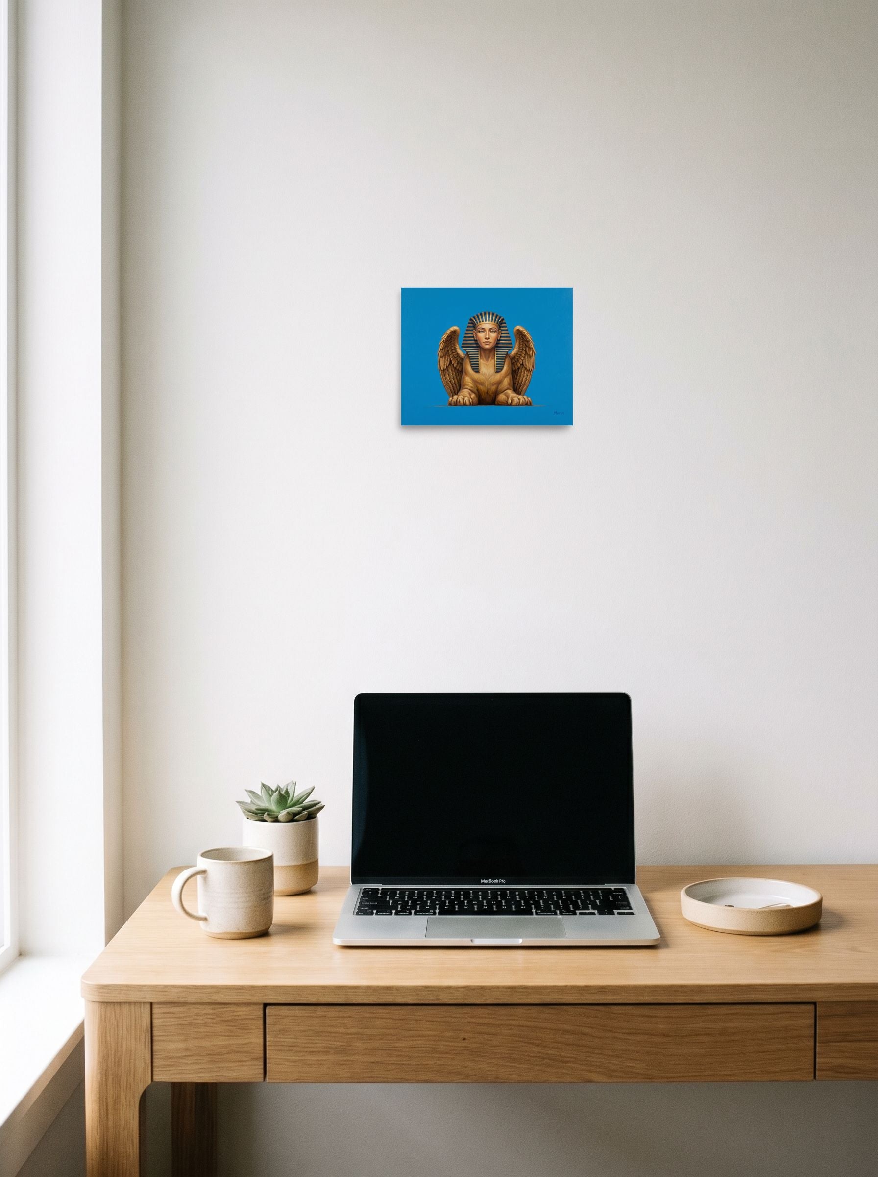 A 10x8 inch unframed paper Realism print of 'The Golden Sphinx' hanging above a worktable with a laptop.