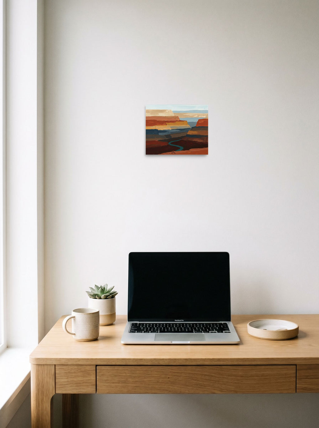 A 10x8 inch unframed paper Expressionism,Impressionism print of 'Deep Canyon River' hanging above a worktable with a laptop.