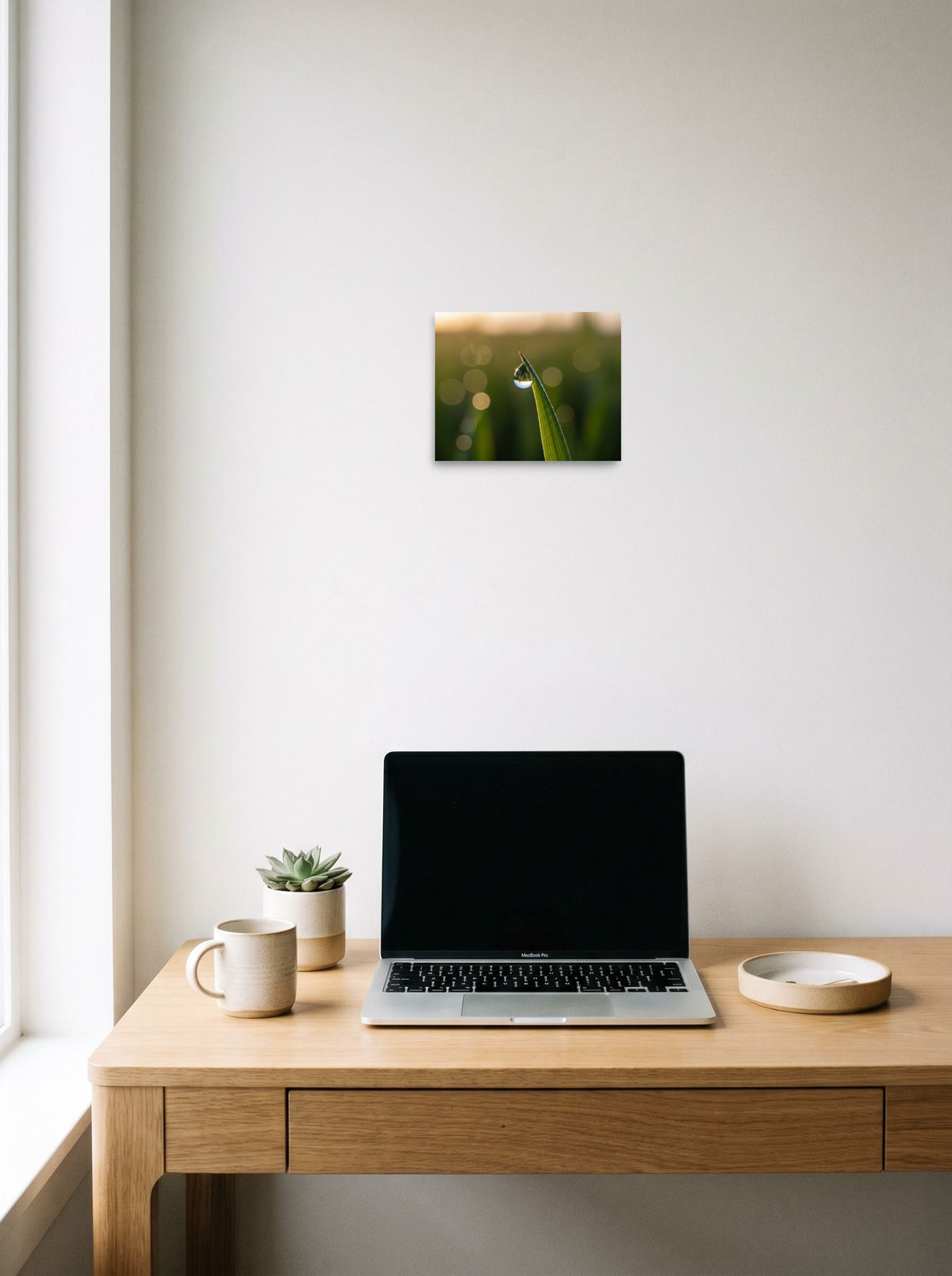 A 10x8 inch unframed paper Art photography print of 'World in a Drop' hanging above a worktable with a laptop.
