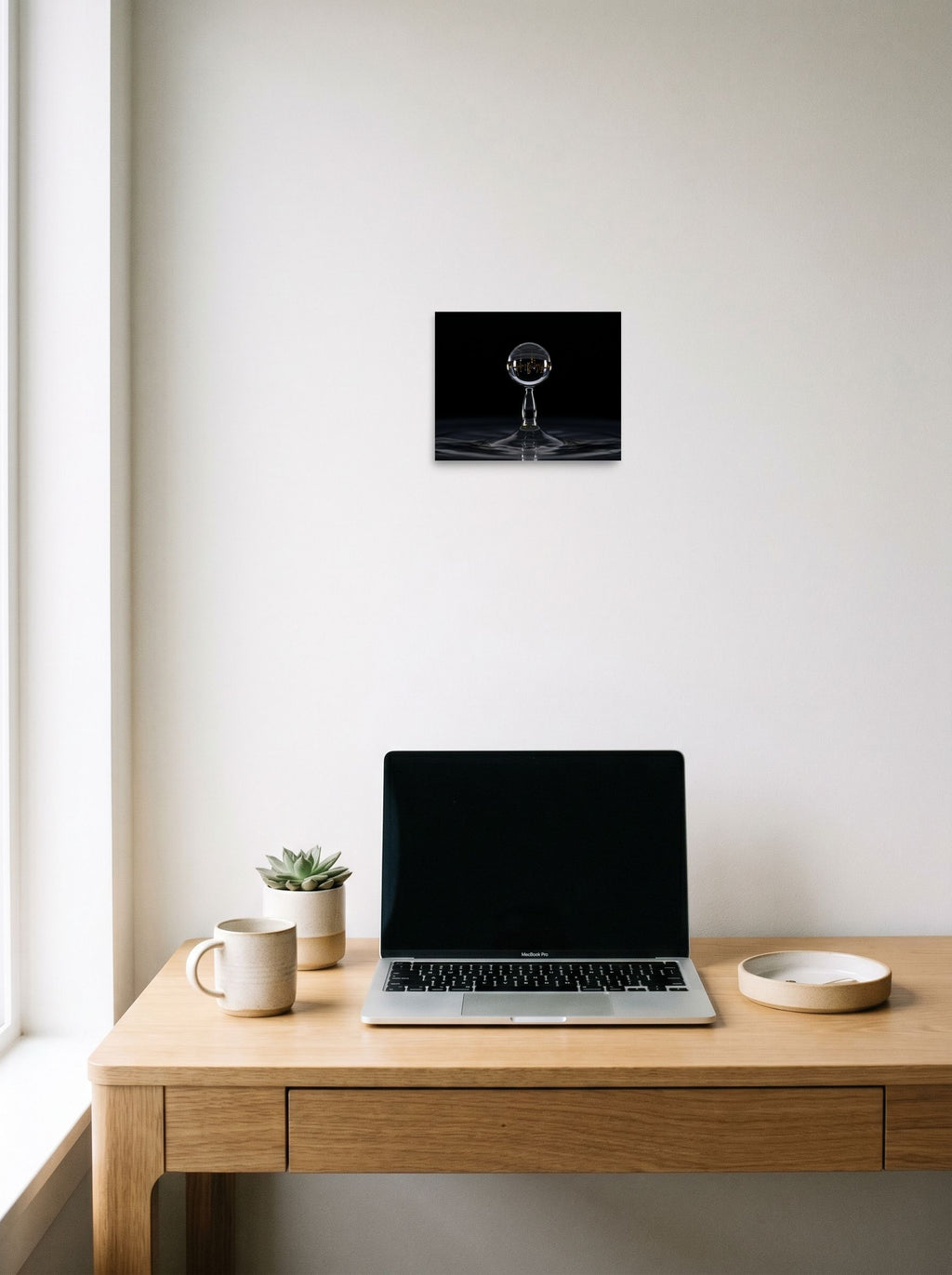 A 10x8 inch unframed paper Surrealism print of 'City in a Drop' hanging above a worktable with a laptop.