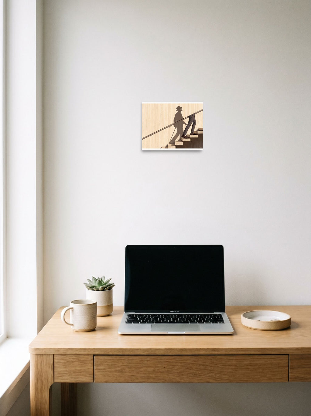 A 10x8 inch unframed paper Surrealism,Realism print of 'Ascent of the Shadow' hanging above a worktable with a laptop.