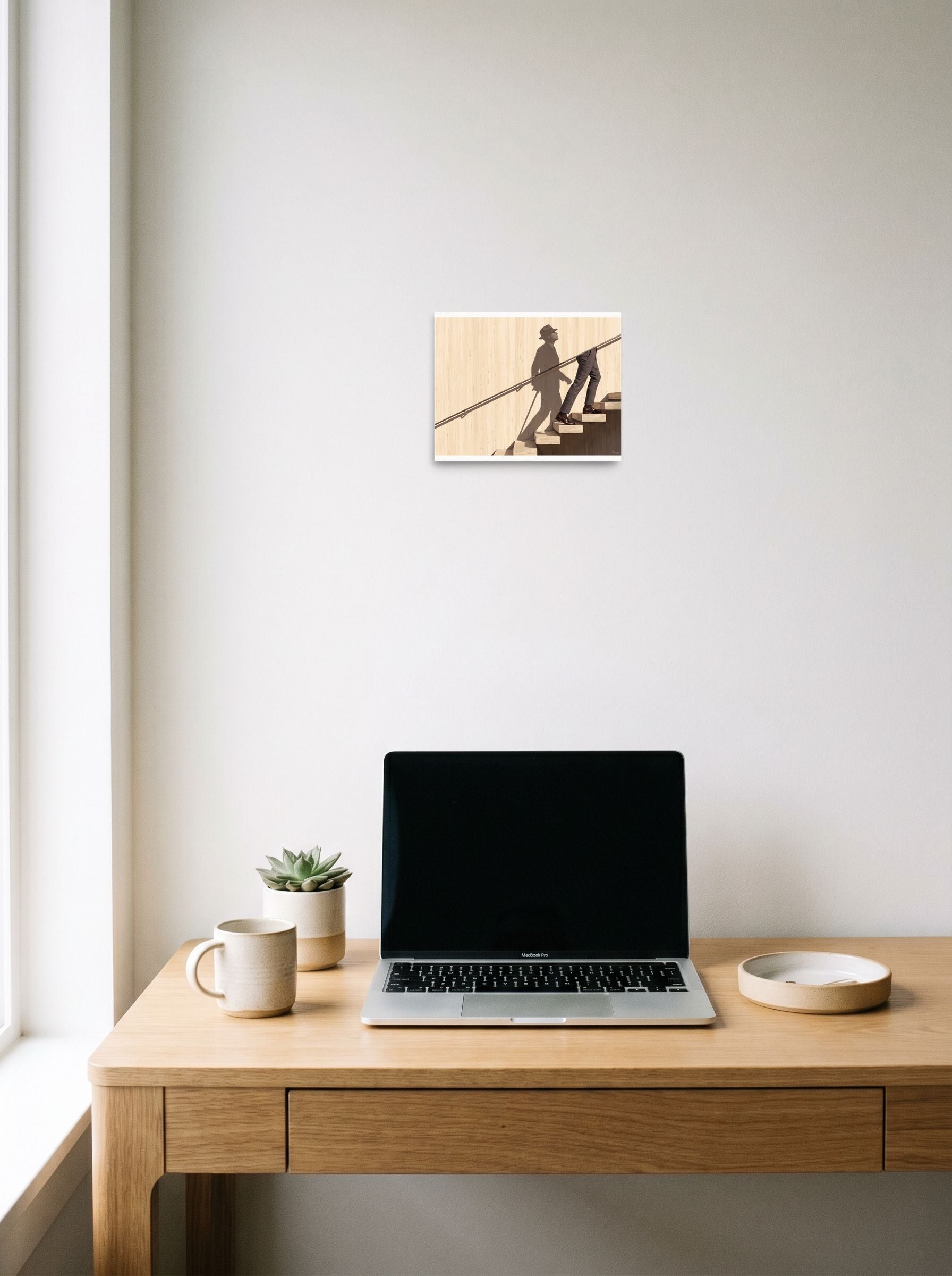 A 10x8 inch unframed paper Surrealism,Realism print of 'Ascent of the Shadow' hanging above a worktable with a laptop.