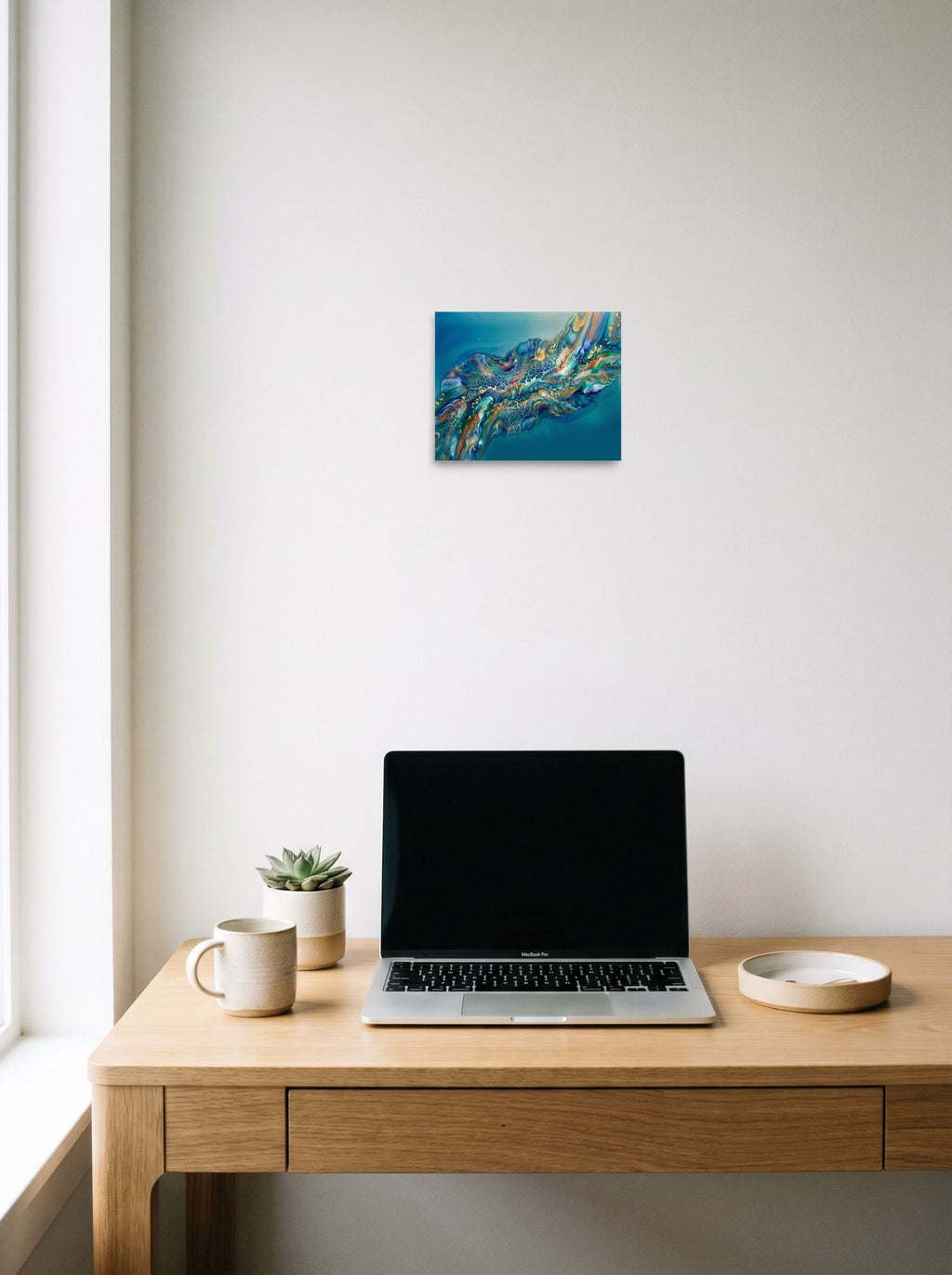 A 10x8 inch unframed paper Abstract art print of 'Teal Nebula' hanging above a worktable with a laptop.