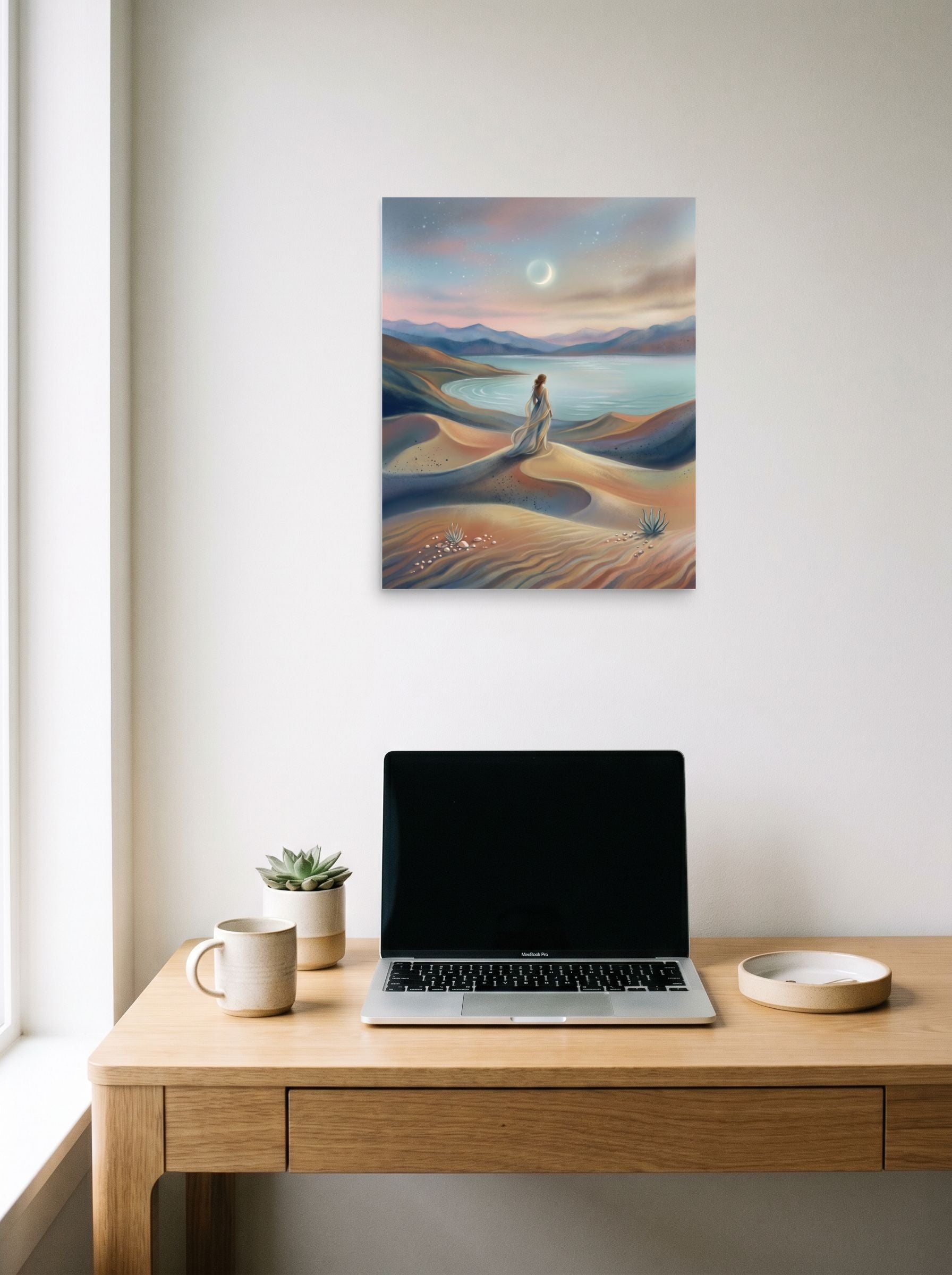A 16x20 inch unframed paper Magic realism print of 'Desert Moonrise' hanging above a worktable with a laptop.