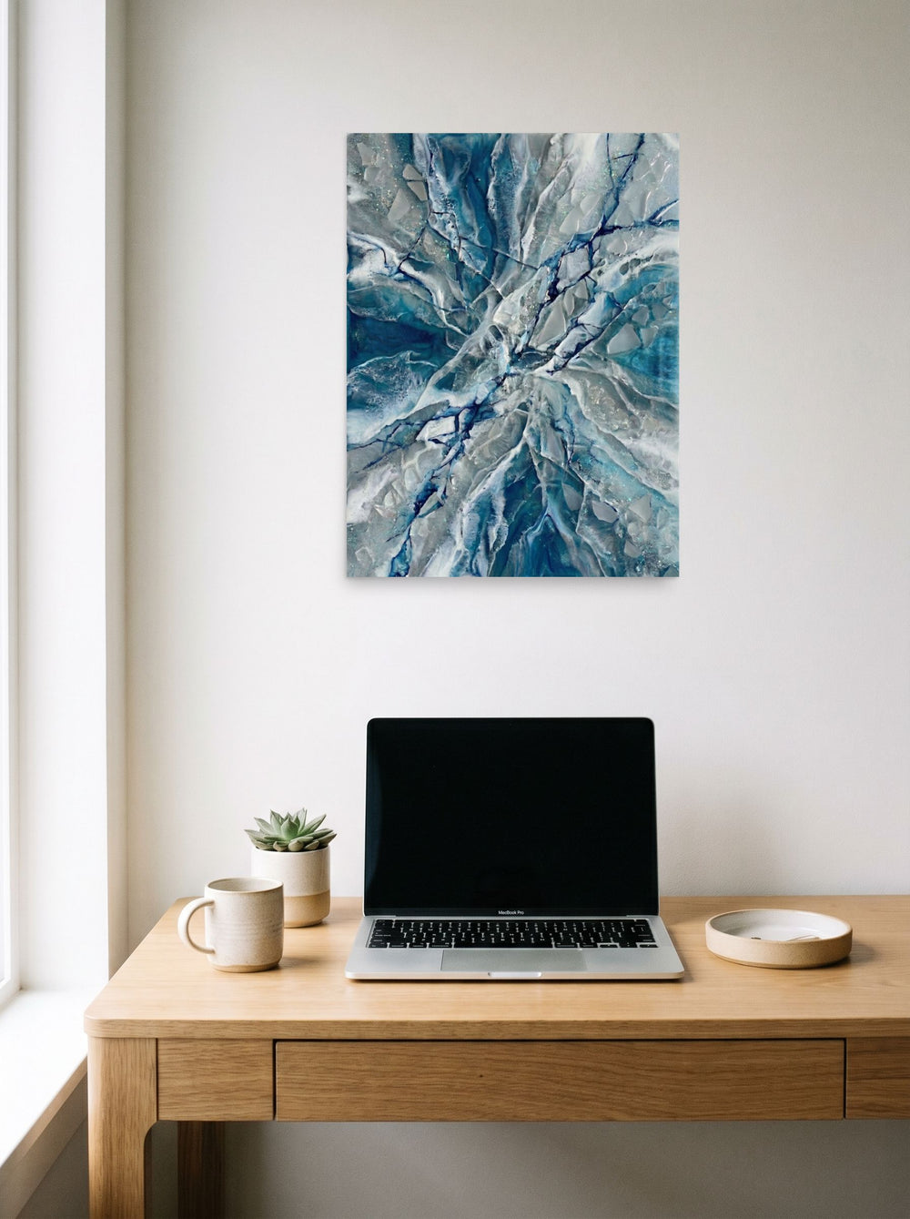 A 18x24 inch unframed paper Abstract art print of 'Shattered Frost' hanging above a worktable with a laptop.