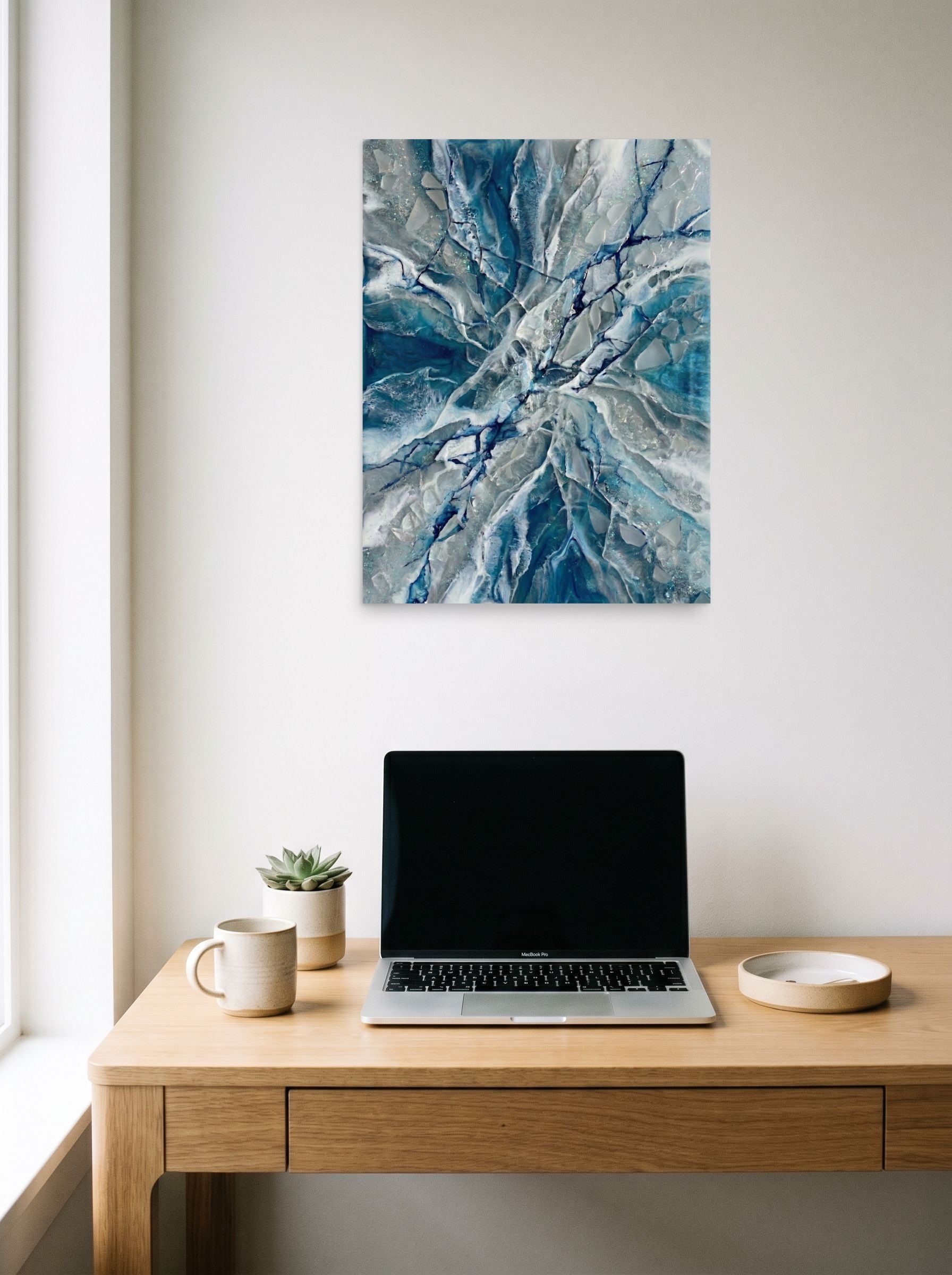 A 18x24 inch unframed paper Abstract art print of 'Shattered Frost' hanging above a worktable with a laptop.