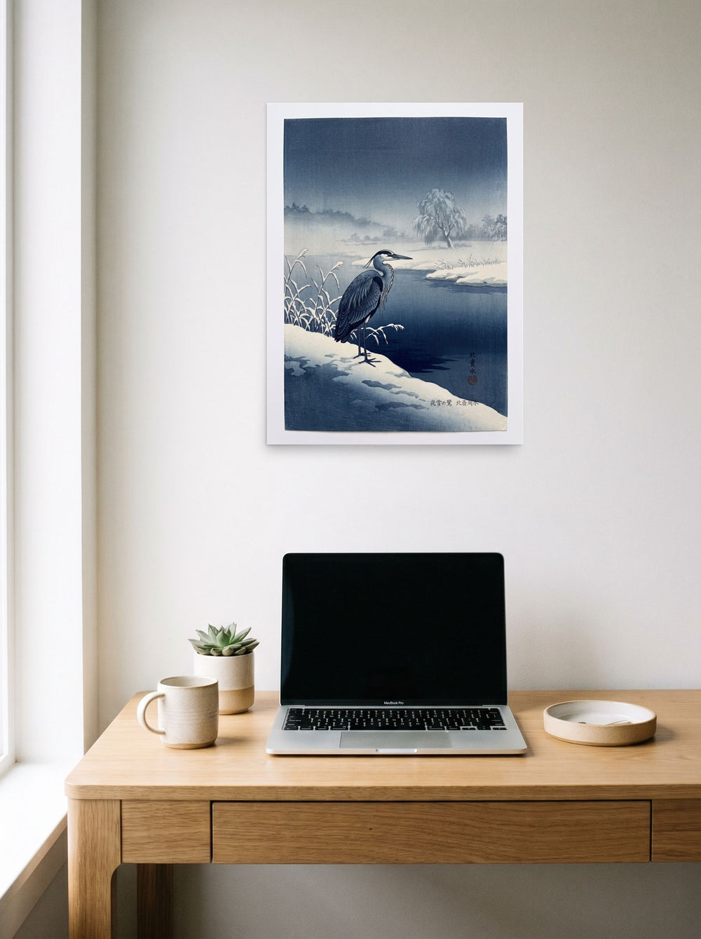A 18x24 inch unframed paper Shin hanga print of 'Winter Heron' hanging above a worktable with a laptop.