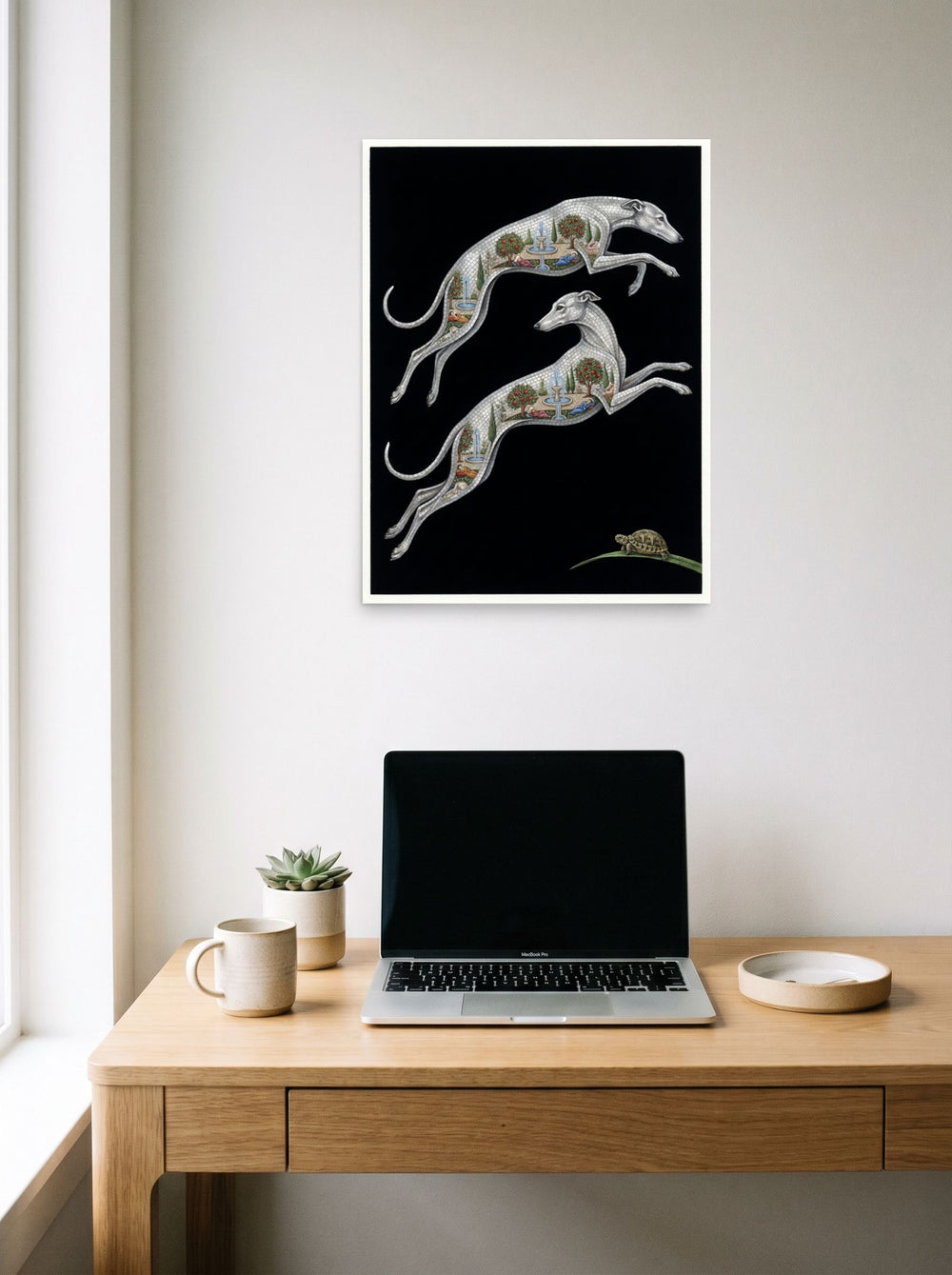 A 18x24 inch unframed paper Art Deco print of 'Greyhound Gardens' hanging above a worktable with a laptop.