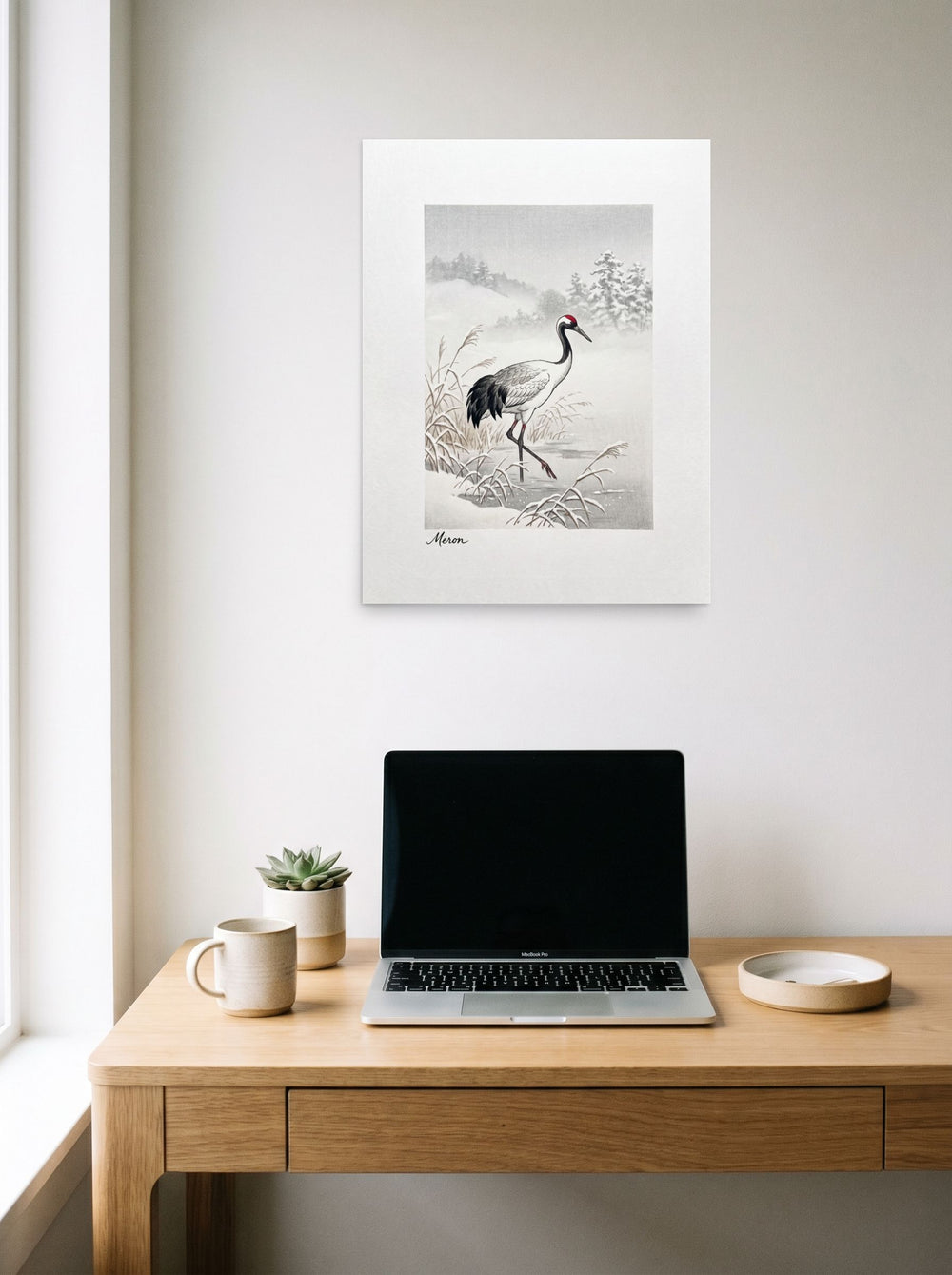 A 18x24 inch unframed paper Shin hanga print of 'Crane in the Frost' hanging above a worktable with a laptop.