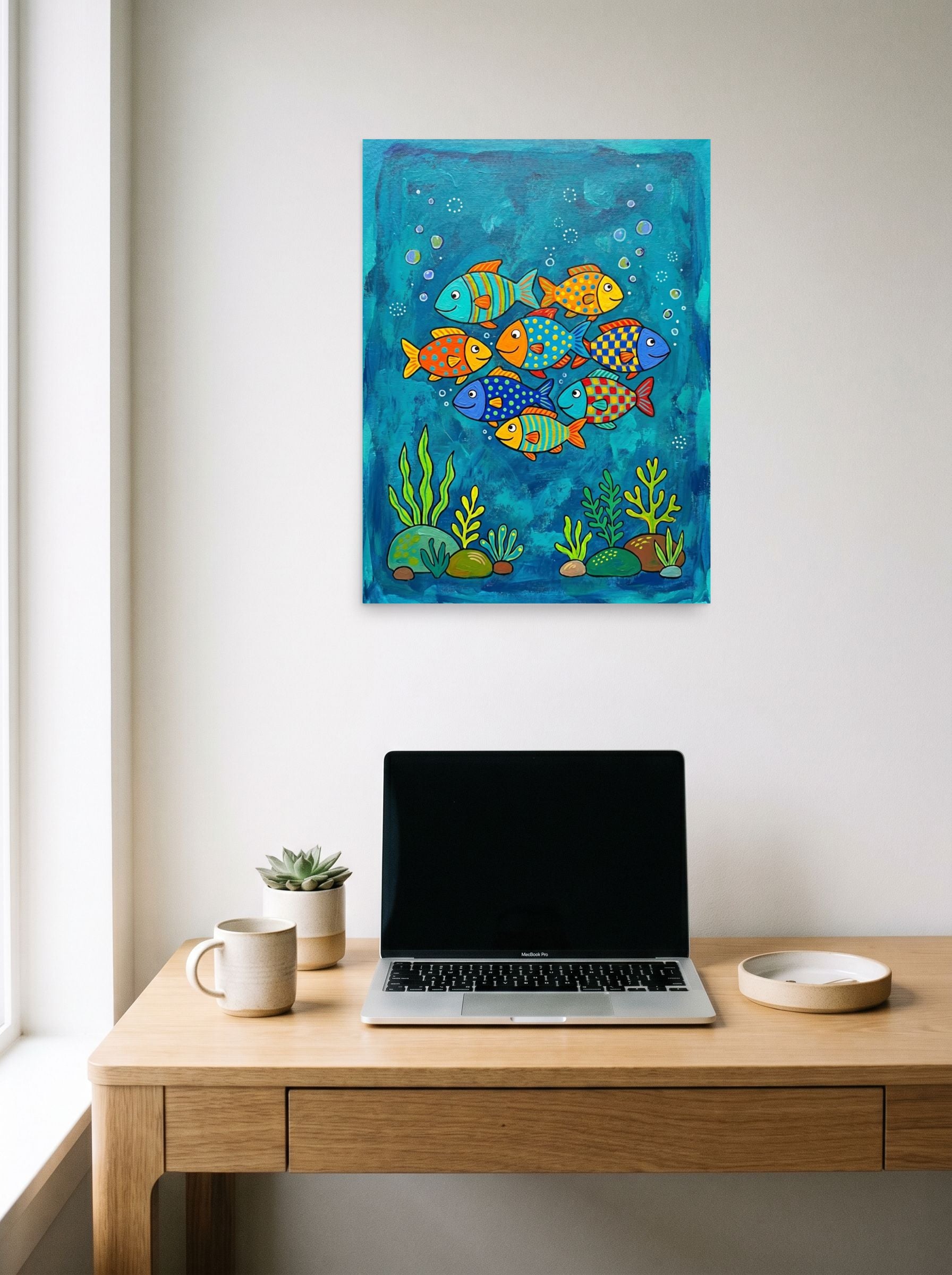A 18x24 inch unframed paper Naive art print of 'Colorful Ocean Friends' hanging above a worktable with a laptop.