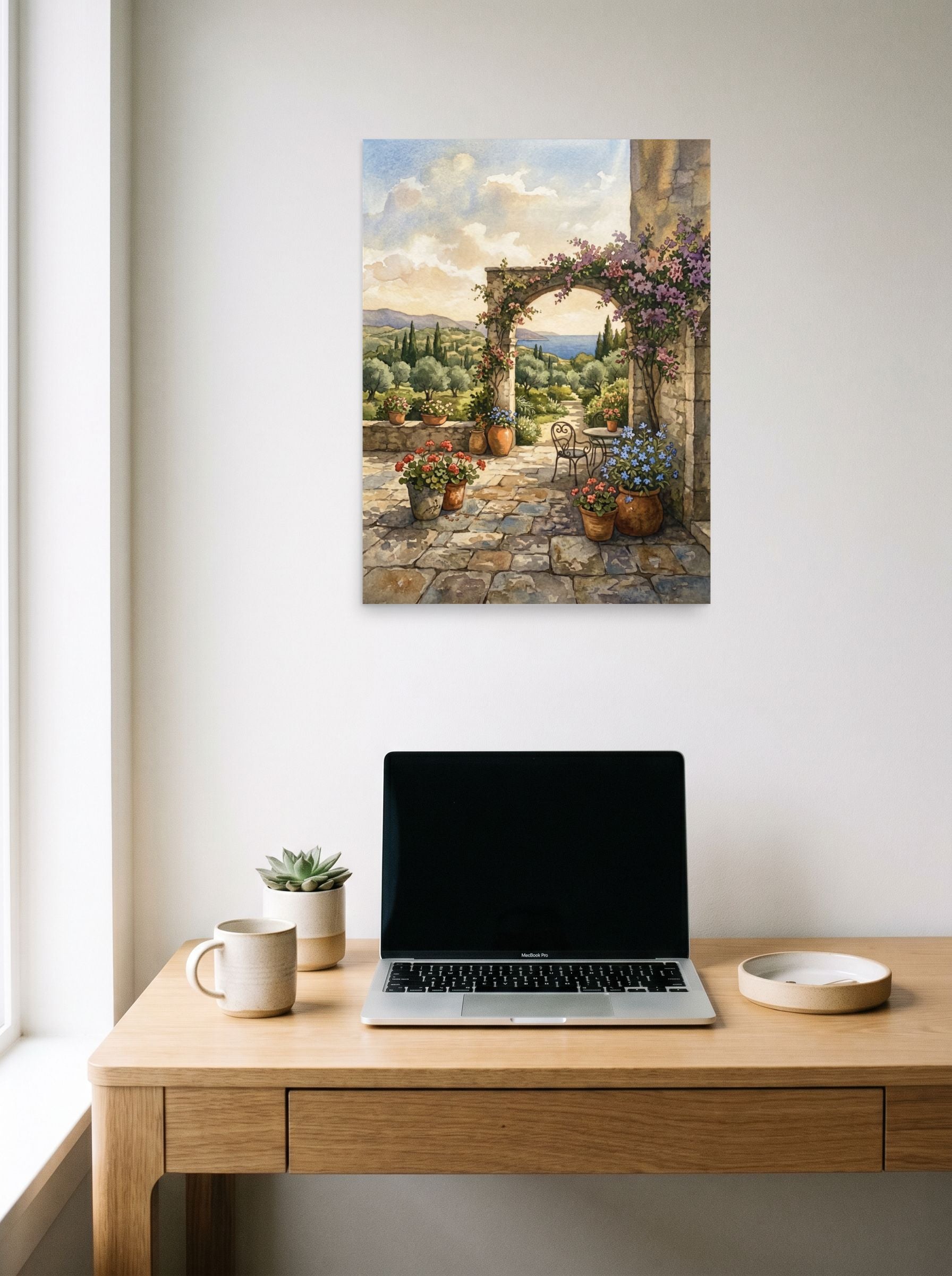 A 18x24 inch unframed paper Realism print of 'Mediterranean Archway' hanging above a worktable with a laptop.