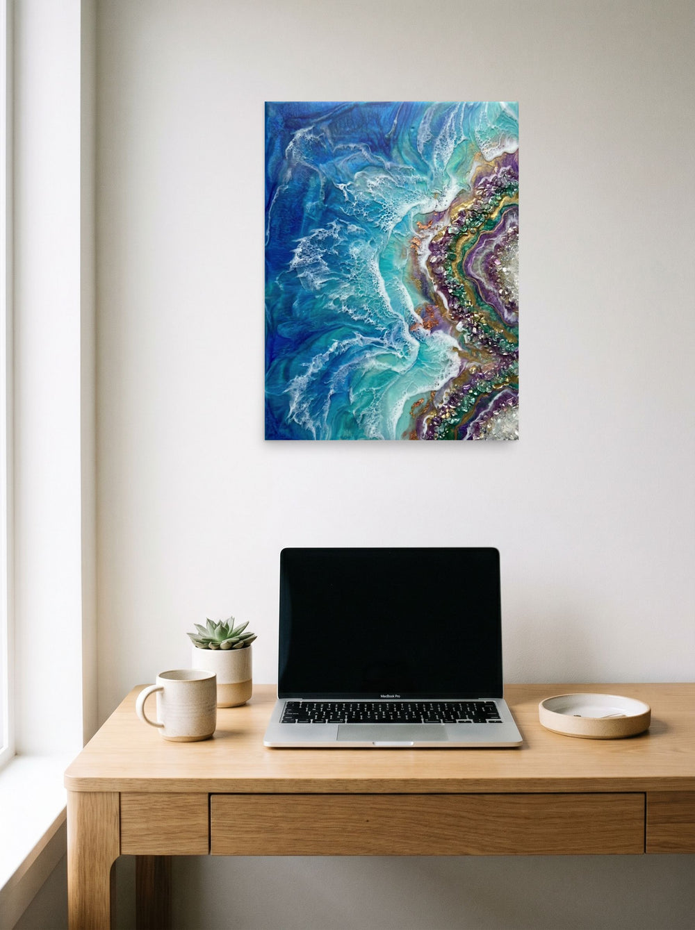 A 18x24 inch unframed paper Abstract art print of 'Crystal Coast' hanging above a worktable with a laptop.
