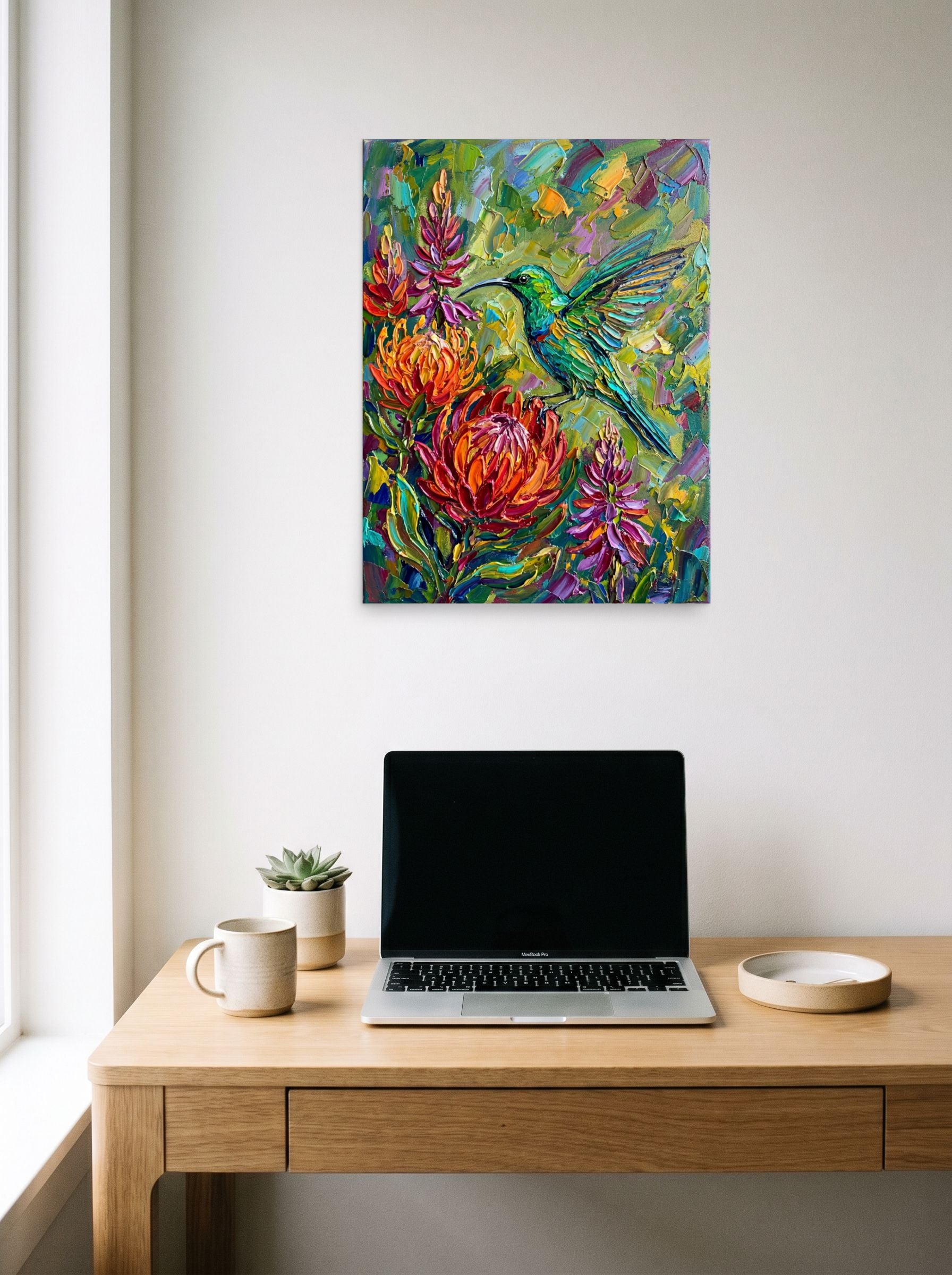 A 18x24 inch unframed paper Impressionism print of 'Emerald Flight Among Proteas' hanging above a worktable with a laptop.