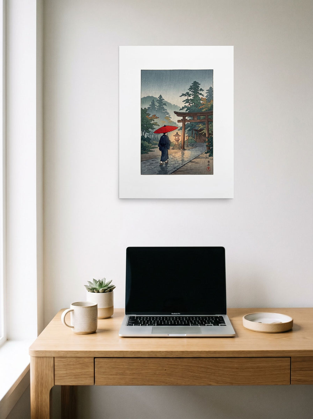 A 18x24 inch unframed paper version of 'Sanctuary in the Rain', Shin hanga wall art, hanging above a worktable with a laptop.