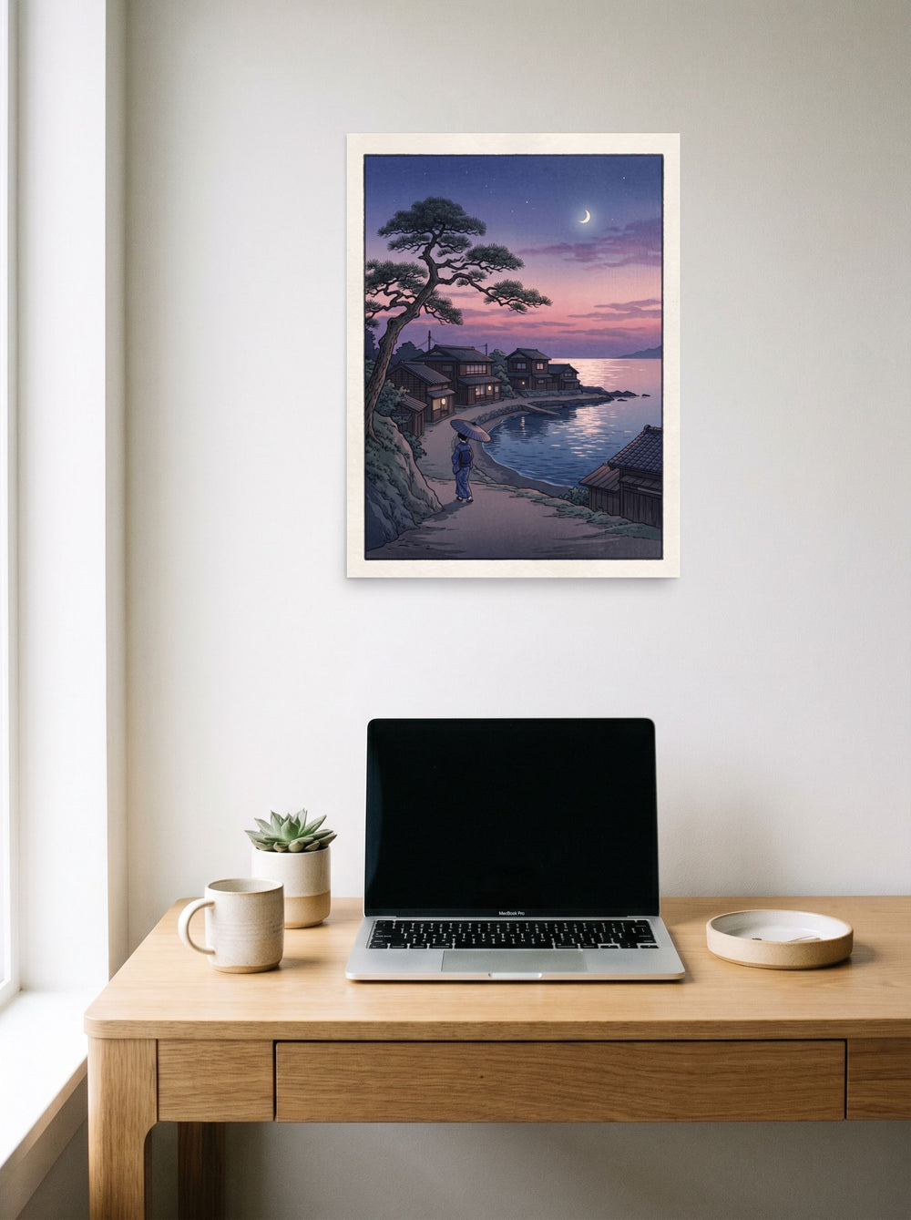 A 18x24 inch unframed paper Shin hanga print of 'Crescent Moon Bay' hanging above a worktable with a laptop.