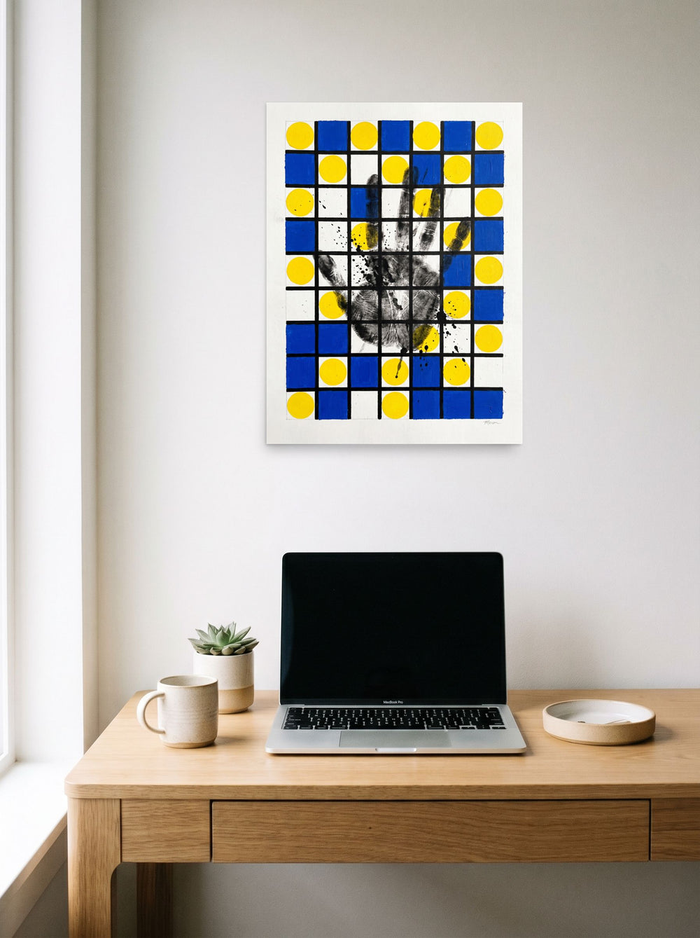 A unframed paper print of the De Stijl (also known as Neoplasticism) artwork 'Human Grid', hanging above a worktable with a laptop.