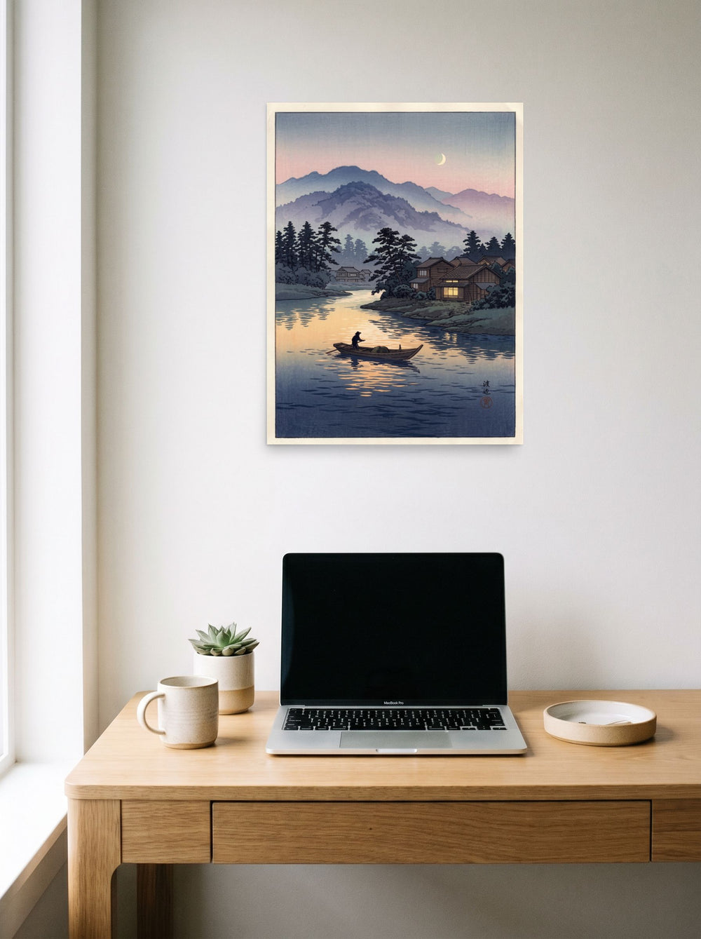 A 18x24 inch unframed paper Shin hanga print of 'Moonlit River Crossing' hanging above a worktable with a laptop.