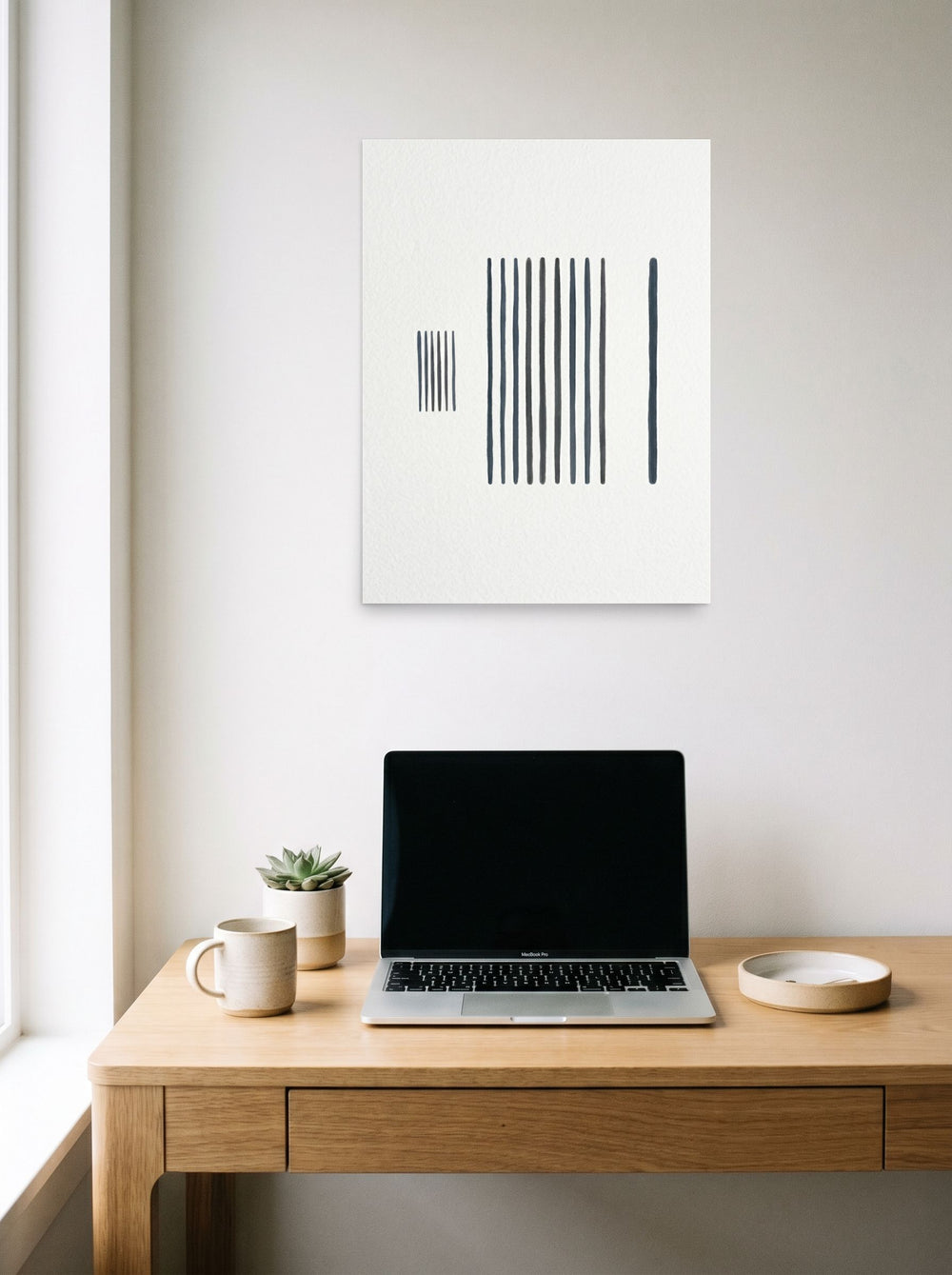 A 18x24 inch unframed paper Minimalism print of 'The Measure of Silence' hanging above a worktable with a laptop.