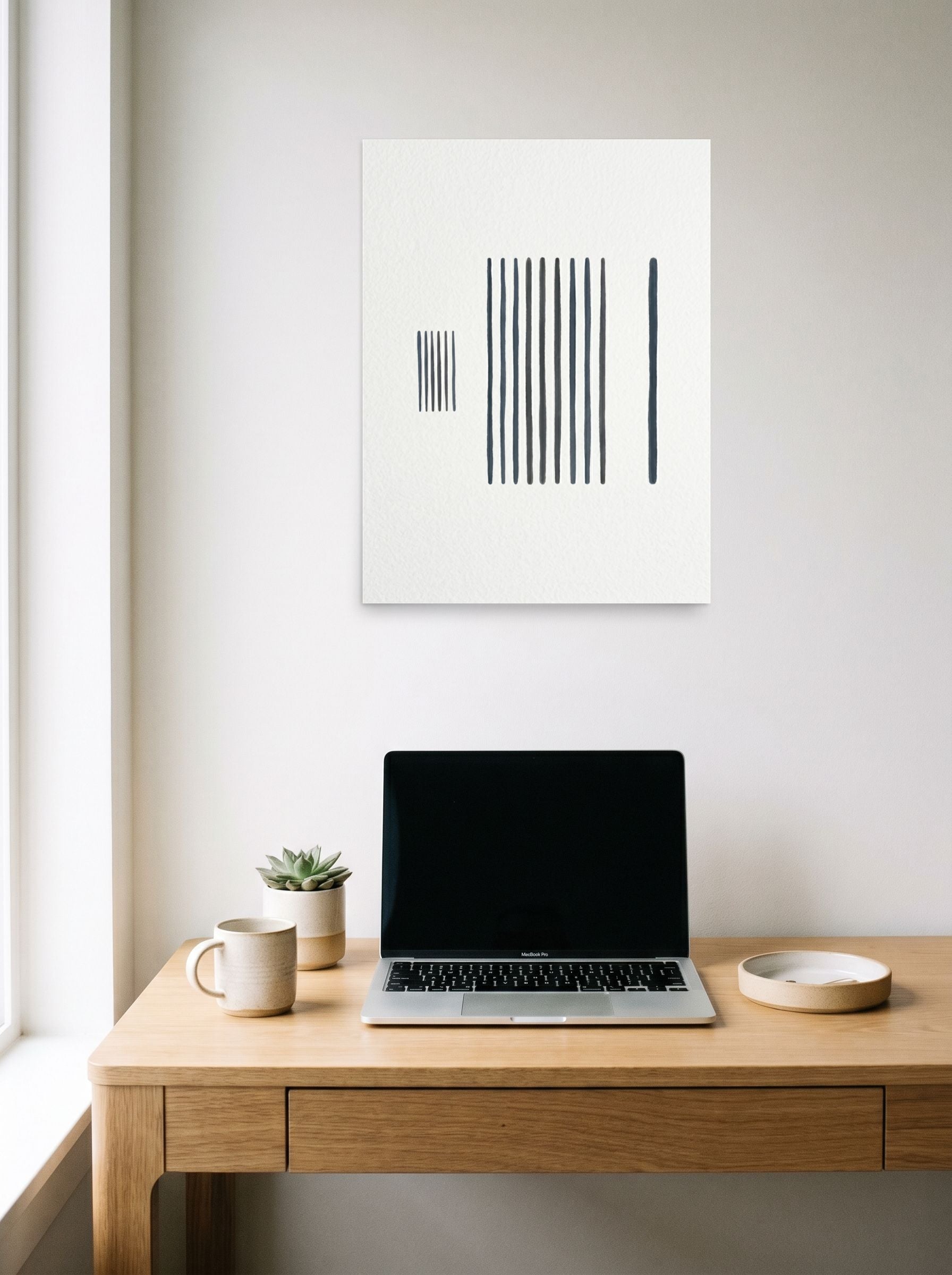A 18x24 inch unframed paper Minimalism print of 'The Measure of Silence' hanging above a worktable with a laptop.