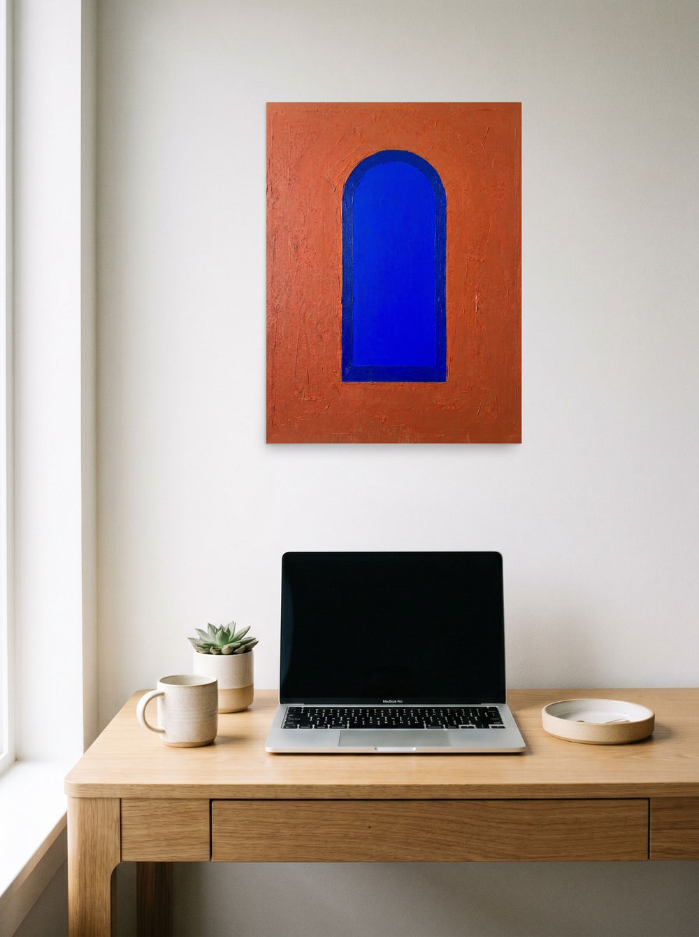 A 18x24 inch unframed paper Minimalism print of 'The Blue Arch' hanging above a worktable with a laptop.