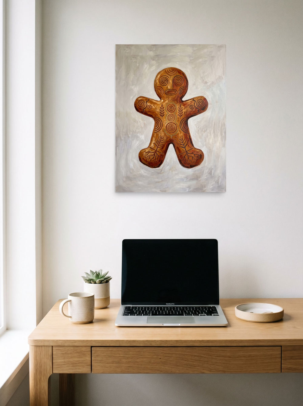 A unframed paper print of the Folk art artwork 'Ancient Gingerbread Totem', hanging above a worktable with a laptop.