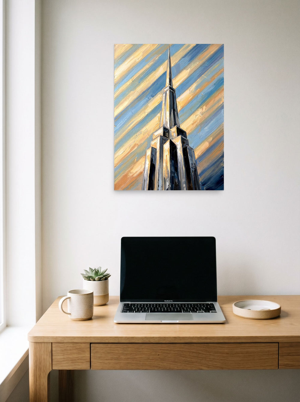 A 18x24 inch unframed paper Art Deco print of 'The Metropolis Spire' hanging above a worktable with a laptop.