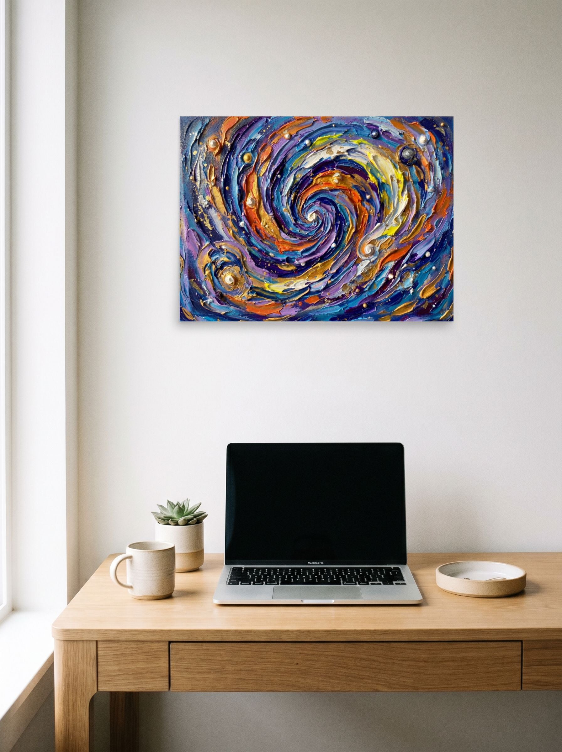 A 24x18 inch unframed paper Abstract expressionism print of 'Cosmic Swirl' hanging above a worktable with a laptop.