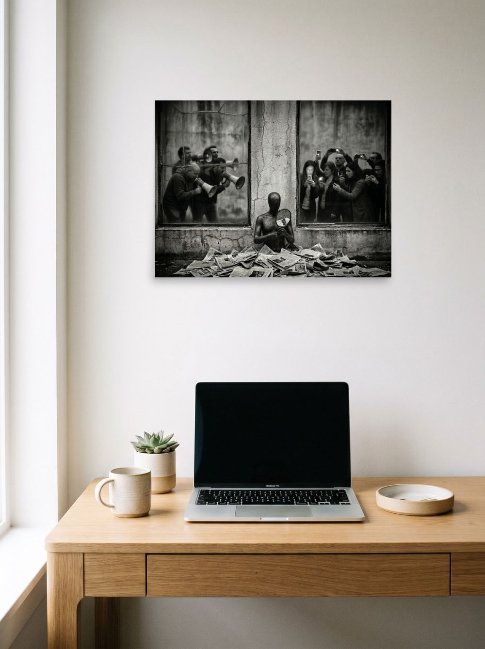 A 24x18 inch unframed paper Surrealism print of 'The Spectacle' hanging above a worktable with a laptop.