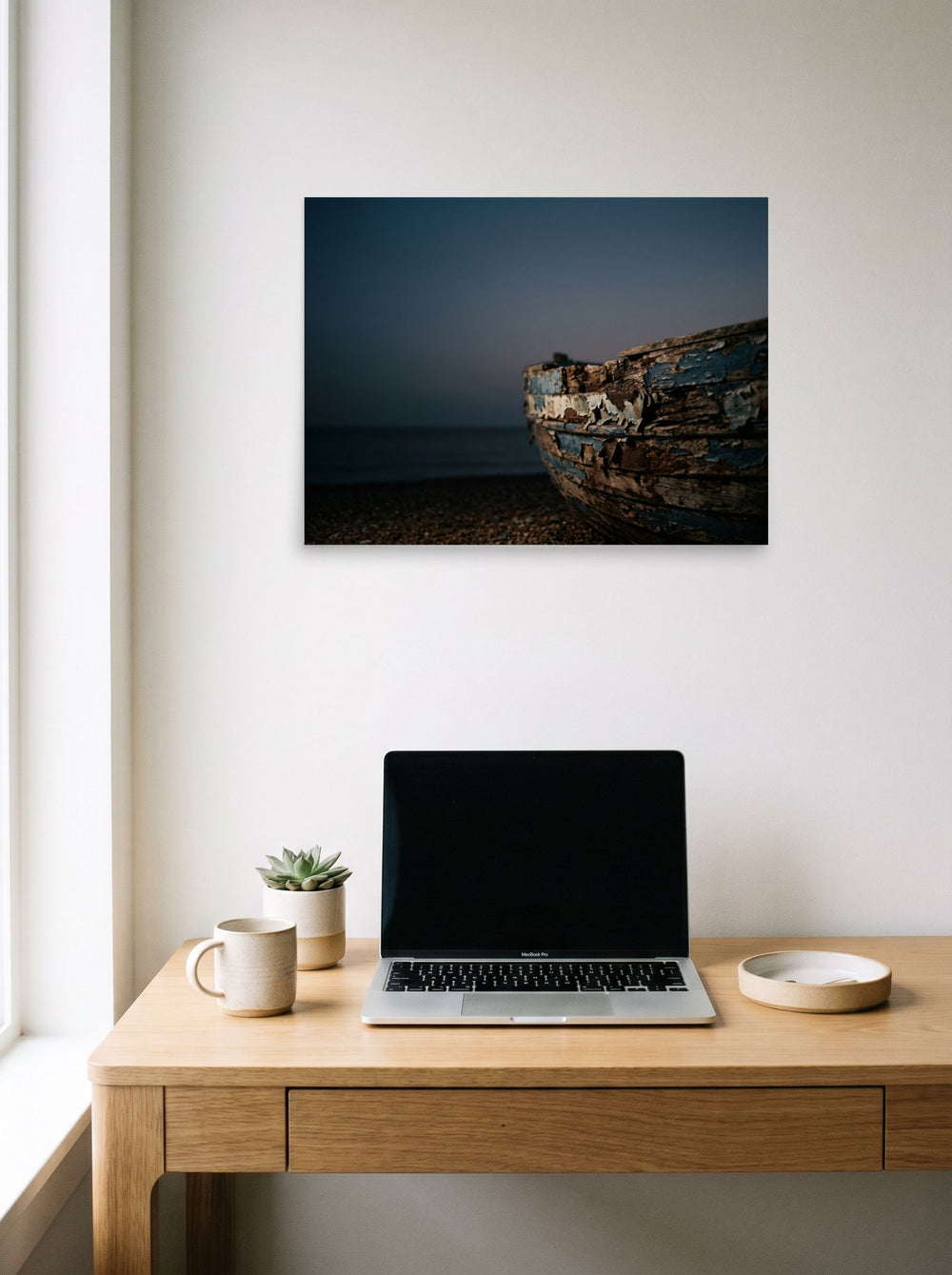 A 24x18 inch unframed paper Art photography print of 'The Faded Blue Boat' hanging above a worktable with a laptop.