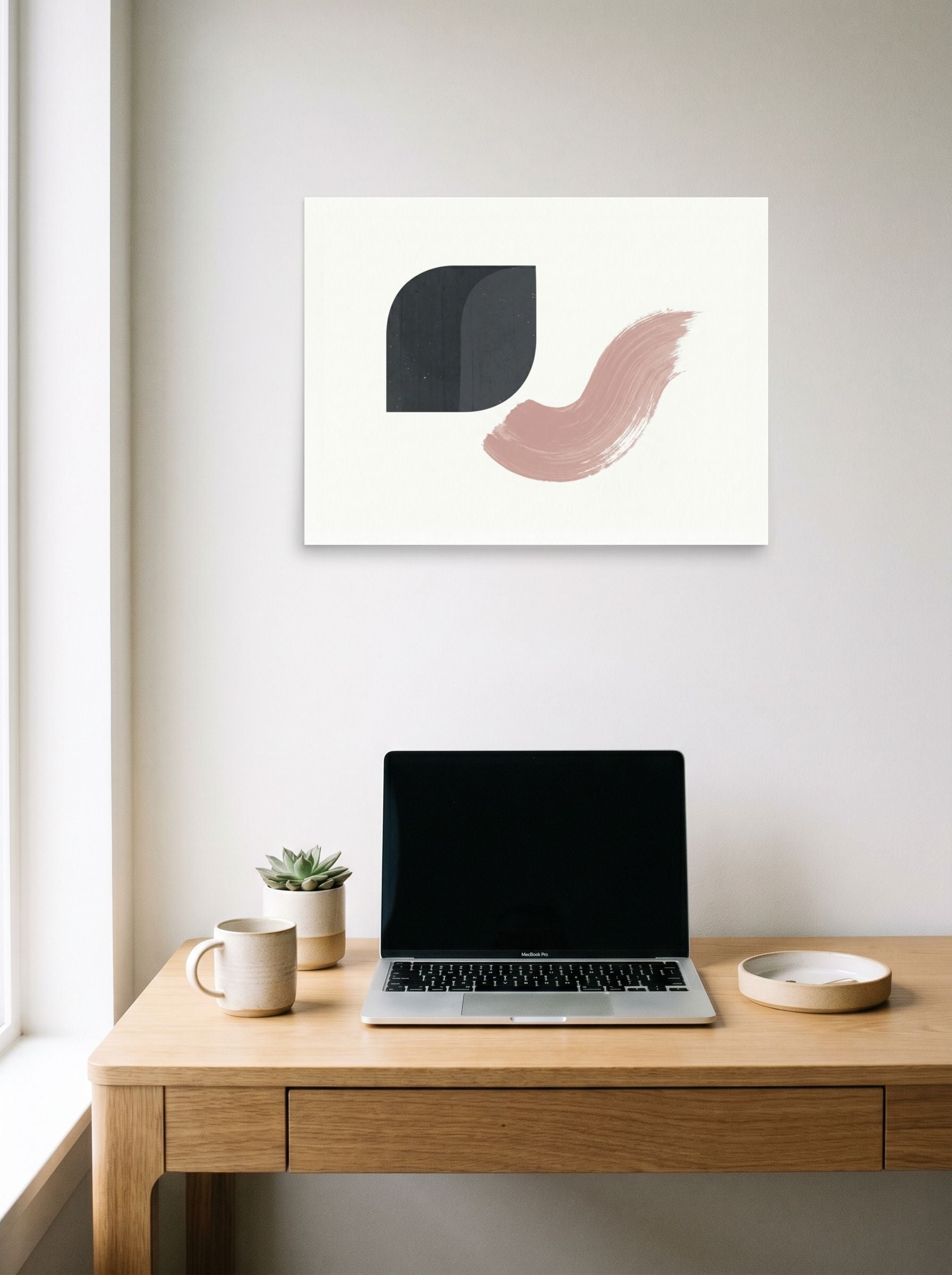 A 24x18 inch unframed paper Minimalism,Geometric abstract art print of 'Geometric Blush' hanging above a worktable with a laptop.
