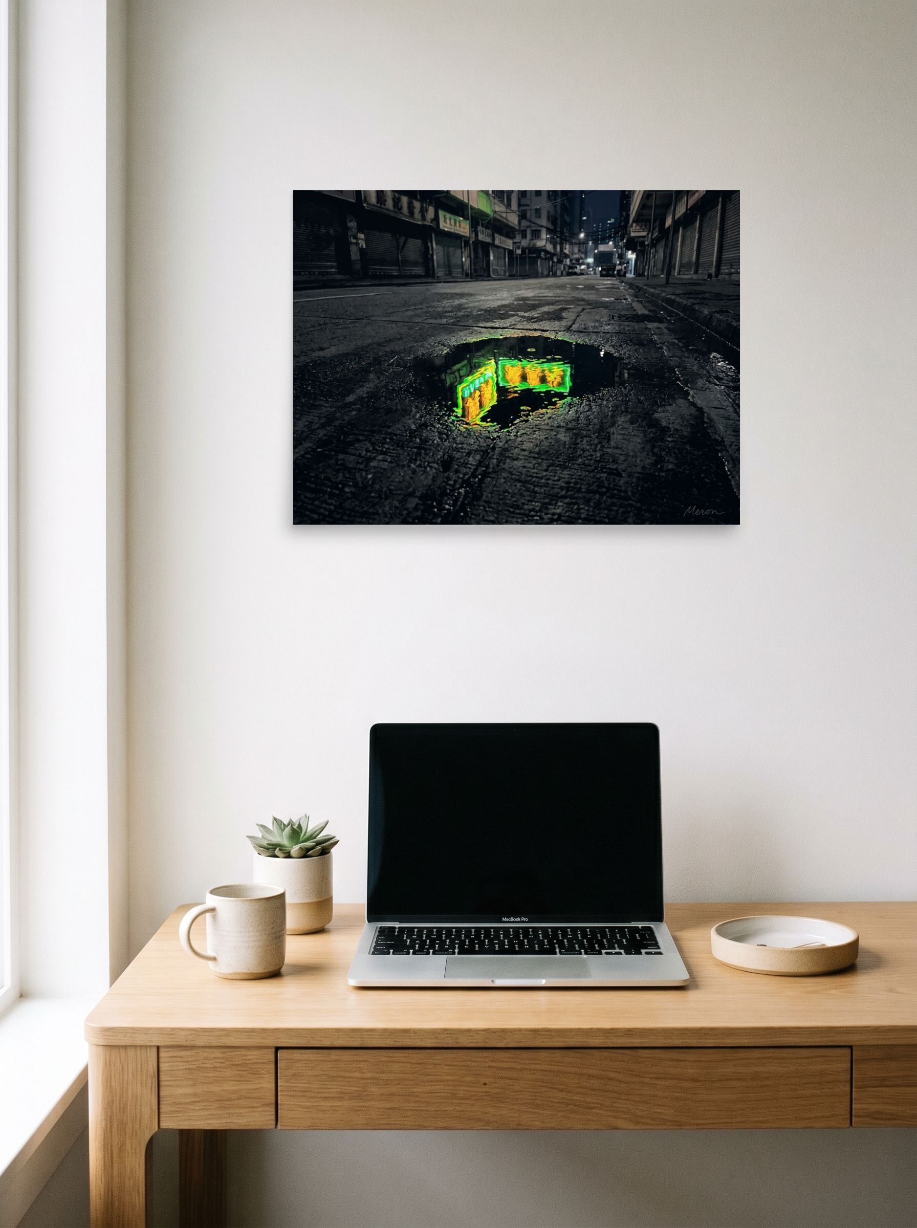 A 24x18 inch unframed paper Photorealism,Street art print of 'Neon Puddle' hanging above a worktable with a laptop.
