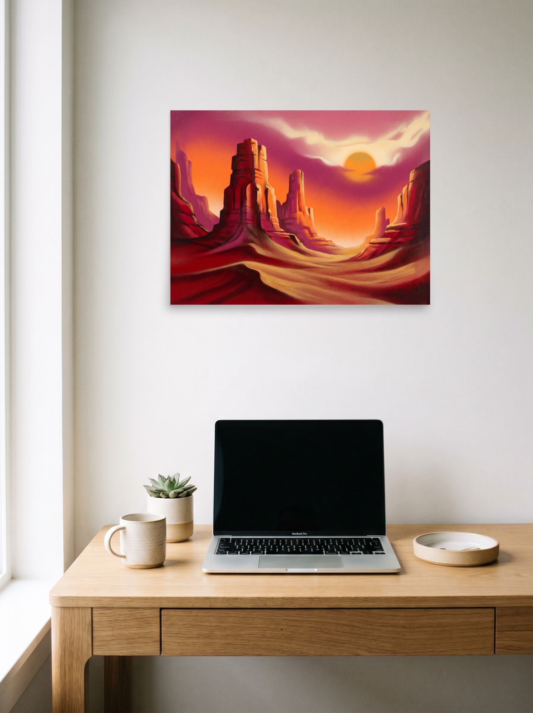 A 24x18 inch unframed paper Realism print of 'Crimson Canyons' hanging above a worktable with a laptop.