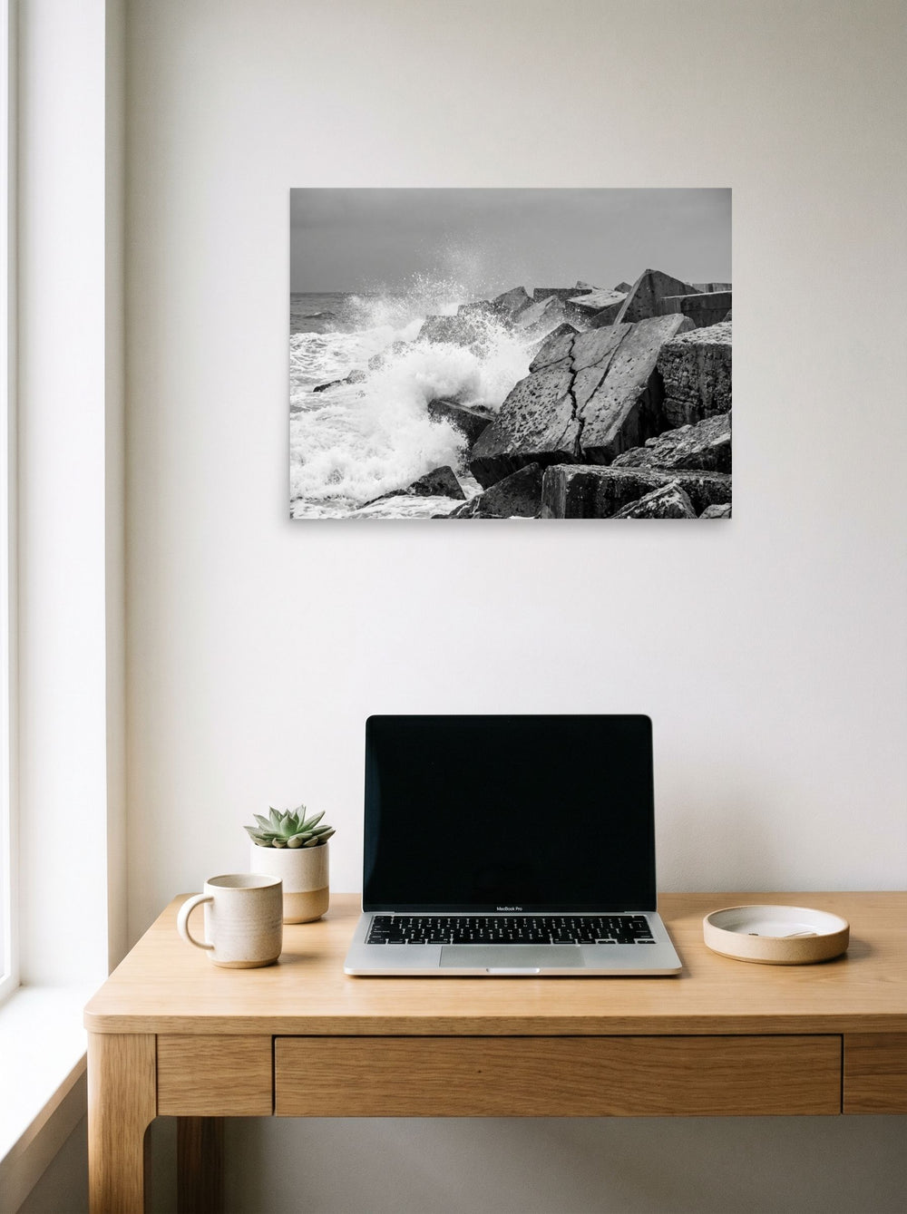 A 24x18 inch unframed paper Art photography print of 'Breakwater Surge' hanging above a worktable with a laptop.