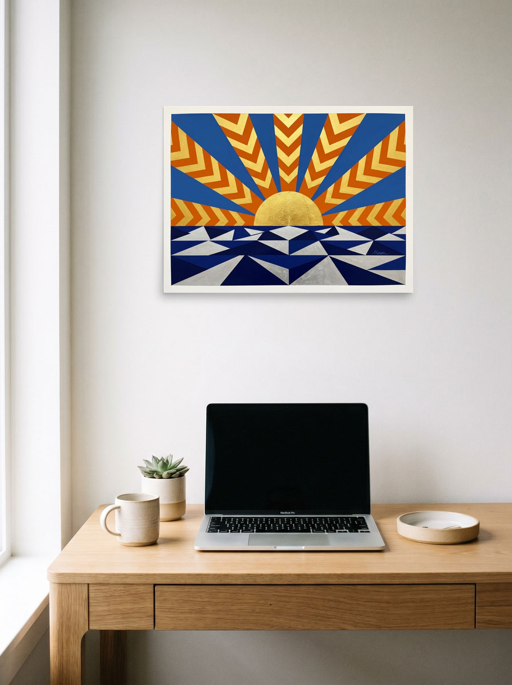 A 24x18 inch unframed paper Art Deco print of 'Deco Sunrise' hanging above a worktable with a laptop.