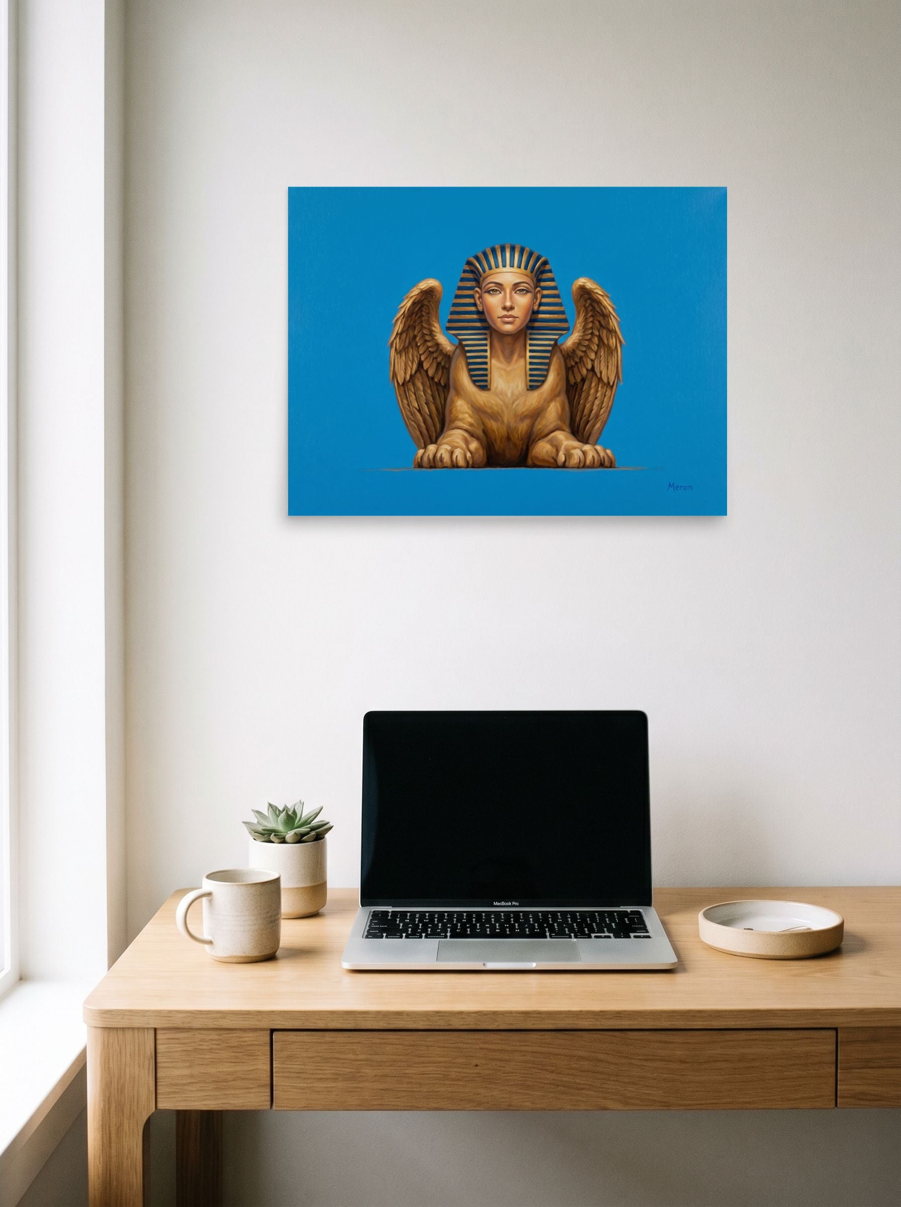 A 24x18 inch unframed paper Realism print of 'The Golden Sphinx' hanging above a worktable with a laptop.