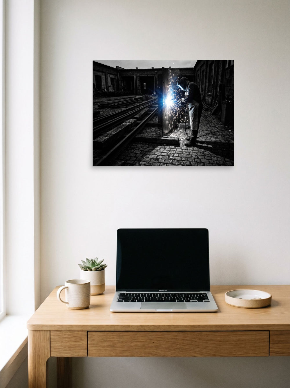 A 24x18 inch unframed paper Art photography print of 'Sparks of Labor' hanging above a worktable with a laptop.