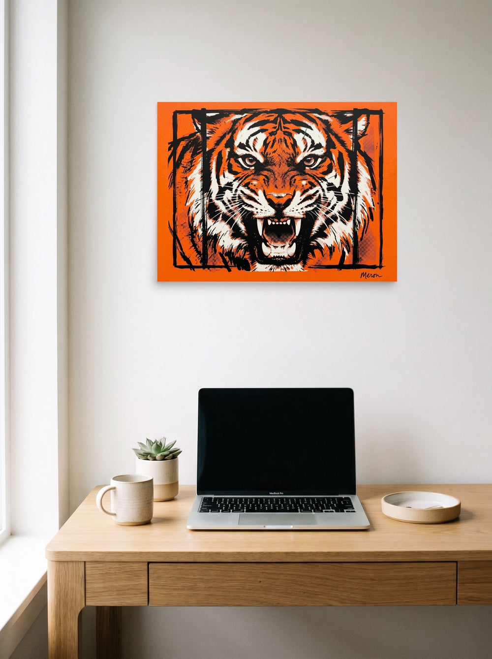 A 24x18 inch unframed paper Pop art print of 'Fierce Roar' hanging above a worktable with a laptop.