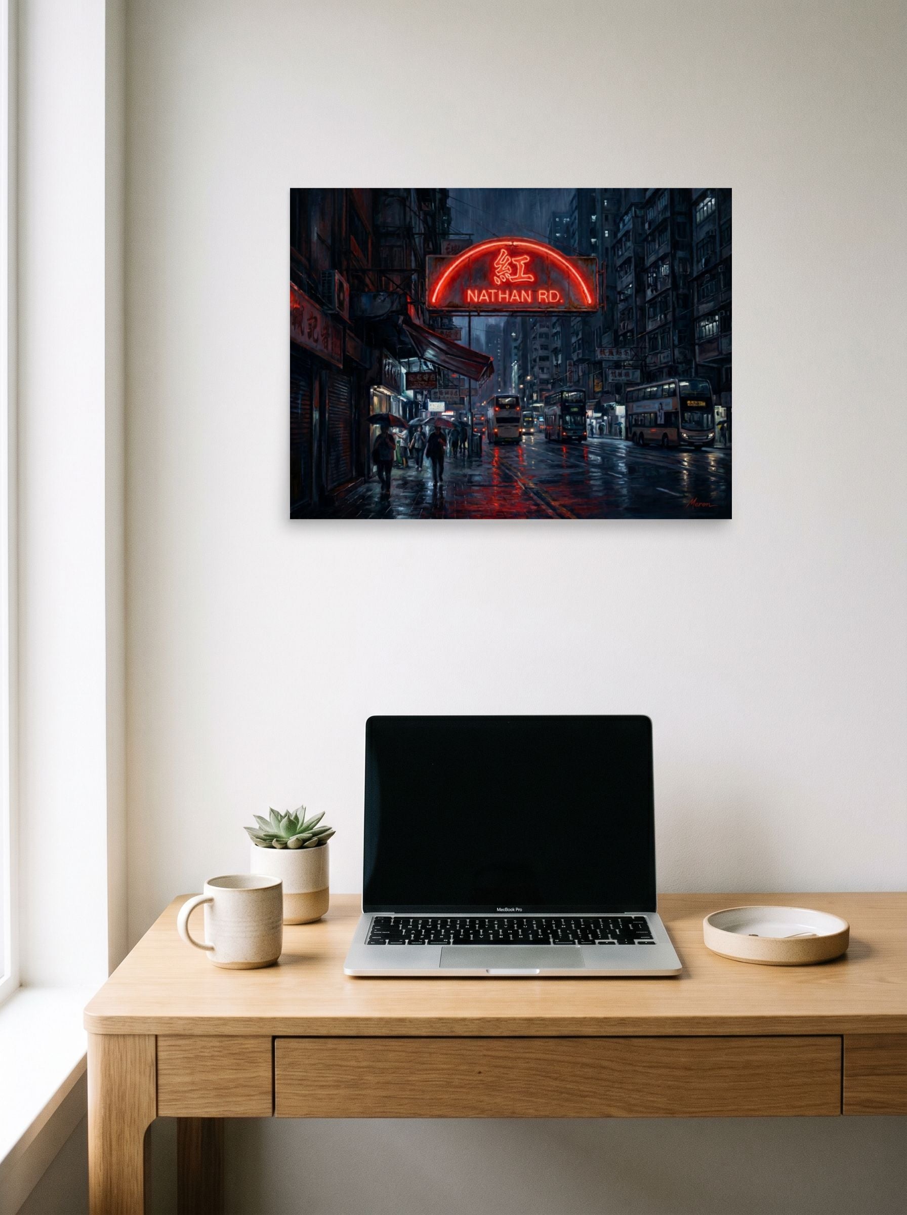 A 24x18 inch unframed paper Realism print of 'Rainy Night on Nathan Road' hanging above a worktable with a laptop.