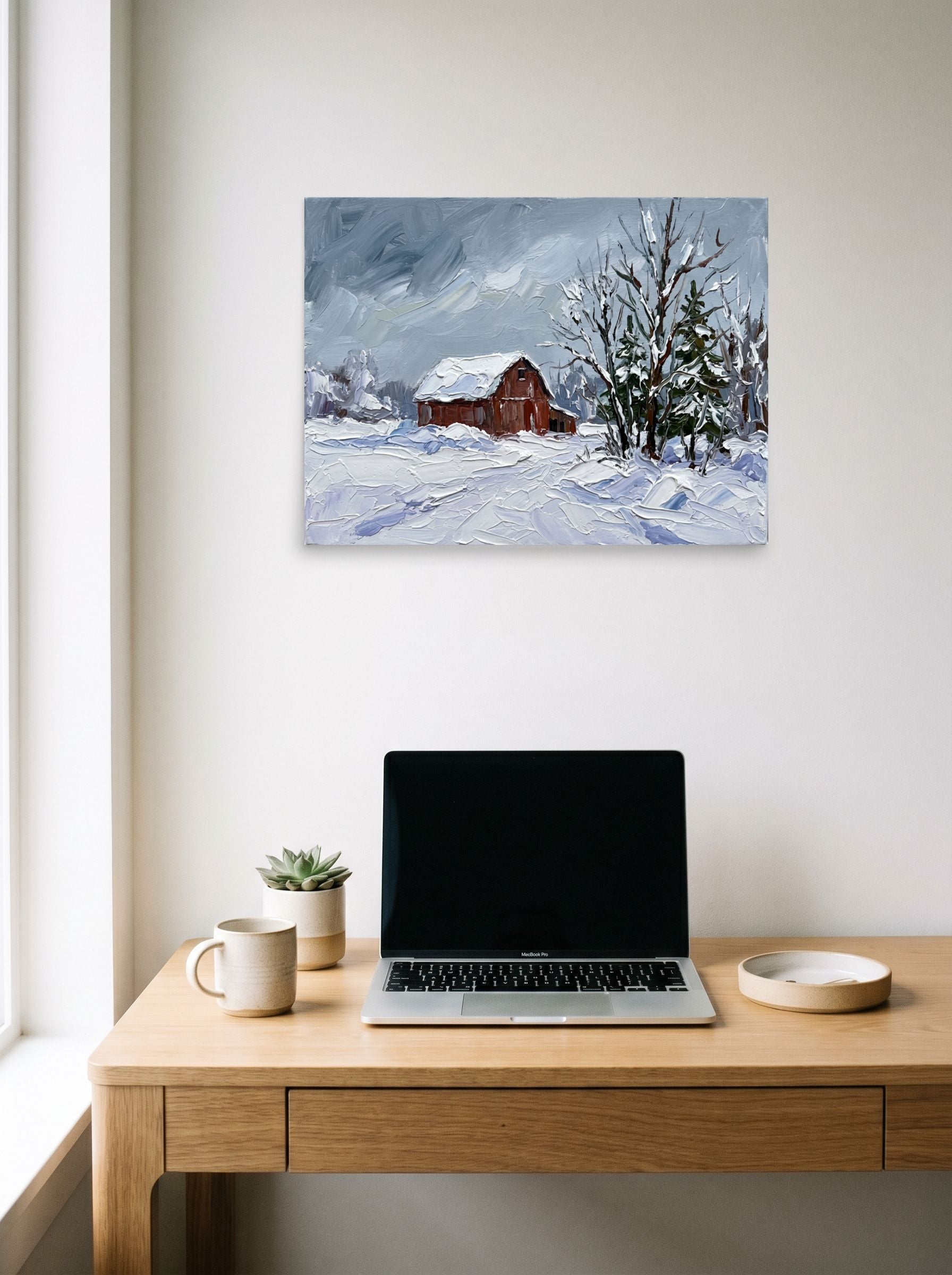 A 24x18 inch unframed paper Impressionism print of 'Winter at the Red Barn' hanging above a worktable with a laptop.