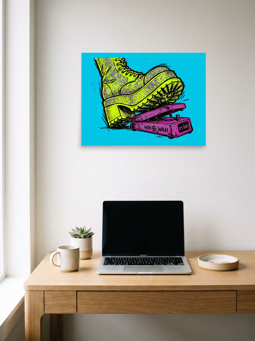A 24x18 inch unframed paper Pop art print of 'Stomp the Fuzz' hanging above a worktable with a laptop.