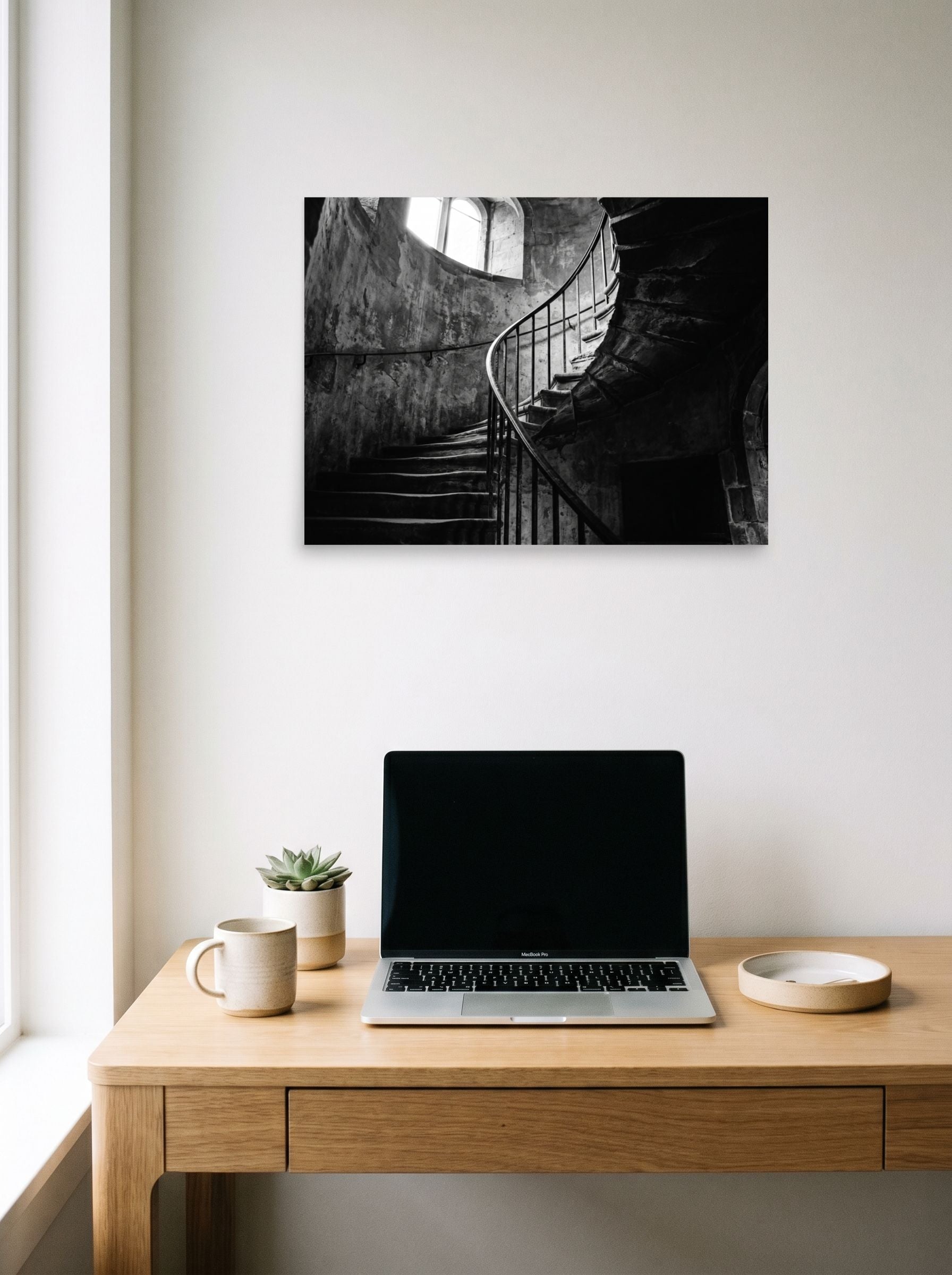 A 24x18 inch unframed paper Art photography print of 'Ascending Shadows' hanging above a worktable with a laptop.