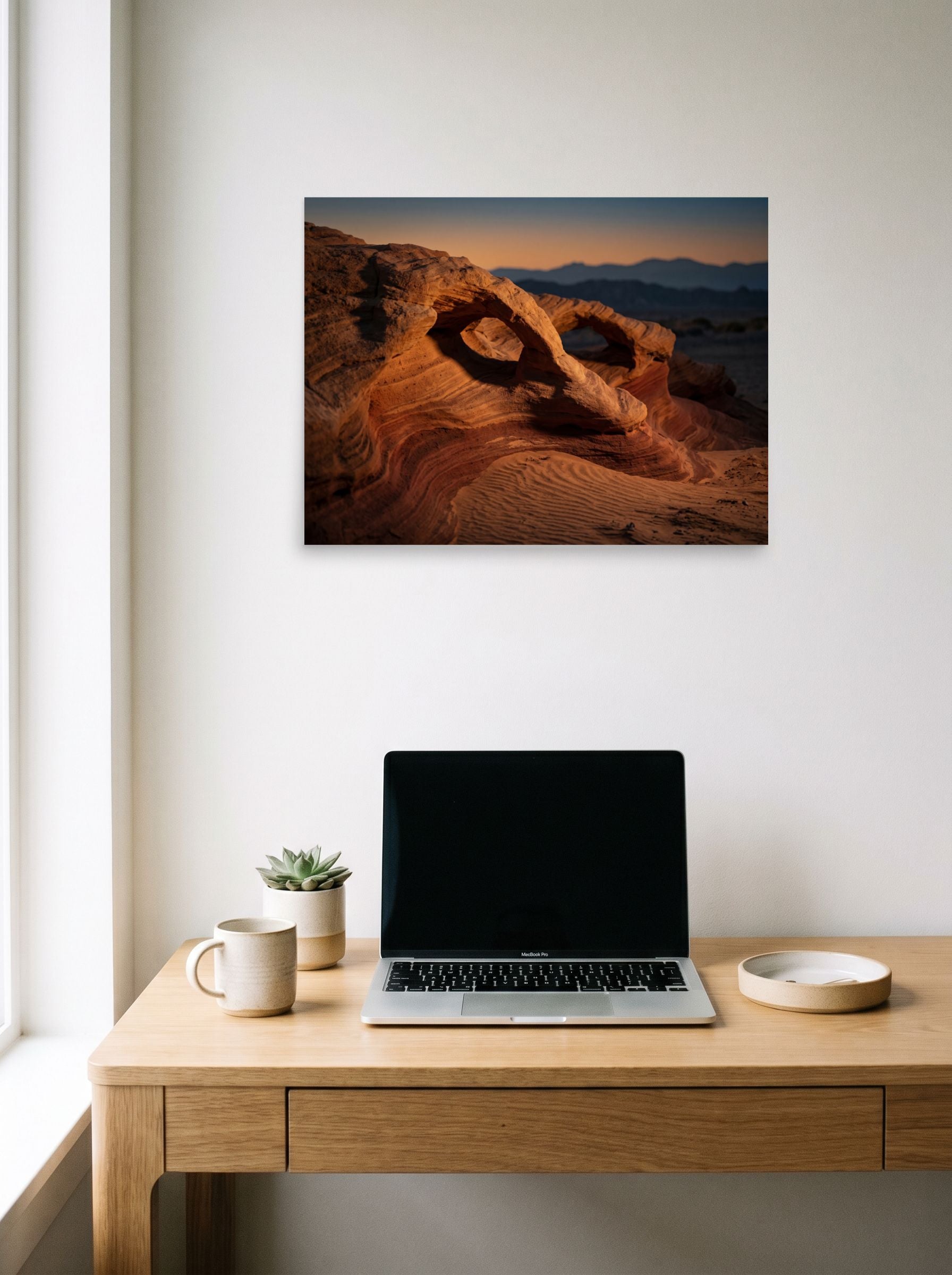 A 24x18 inch unframed paper Art photography print of 'Desert Whispers' hanging above a worktable with a laptop.