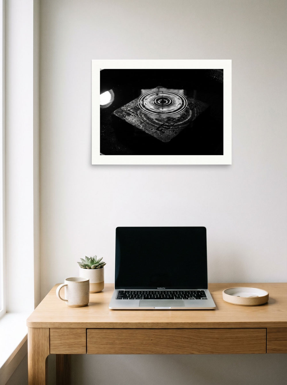 A 24x18 inch unframed paper Art photography print of 'Concentric Resonance' hanging above a worktable with a laptop.
