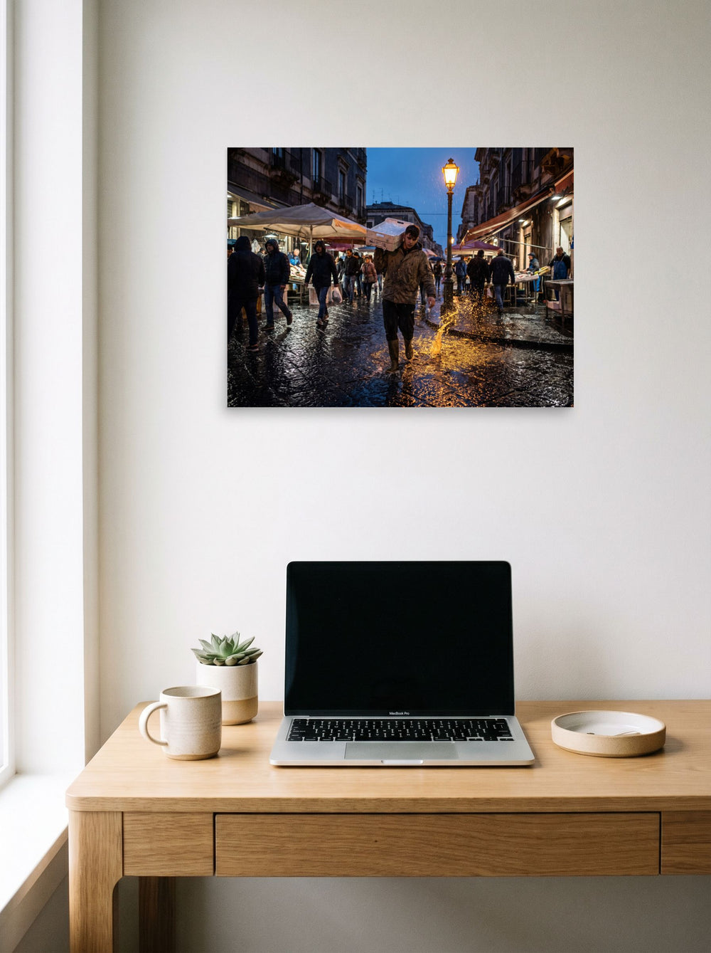A 24x18 inch unframed paper Art photography print of 'Market Rain at Dusk' hanging above a worktable with a laptop.