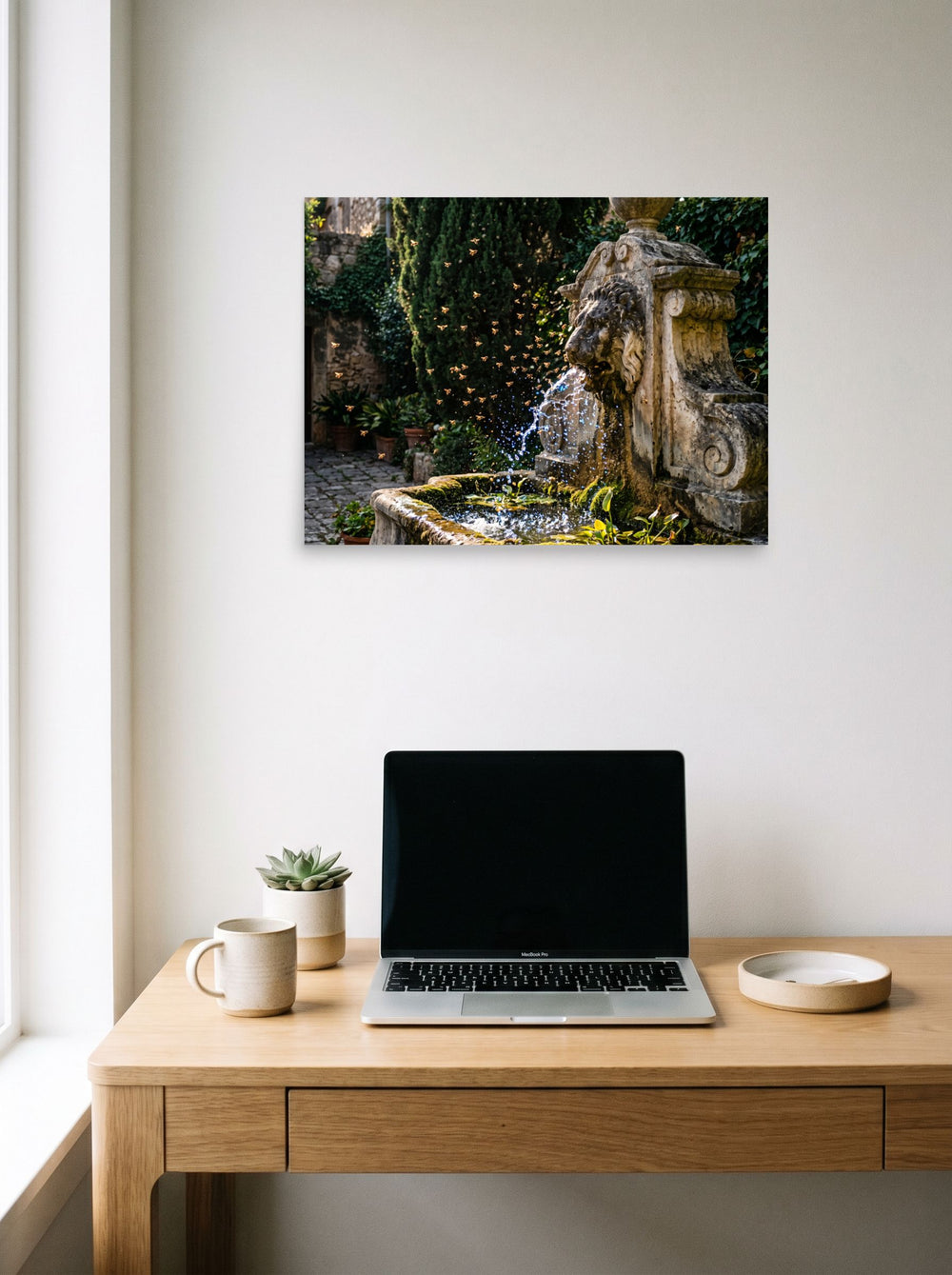 A 24x18 inch unframed paper Art photography print of 'Fountain of the Swarm' hanging above a worktable with a laptop.